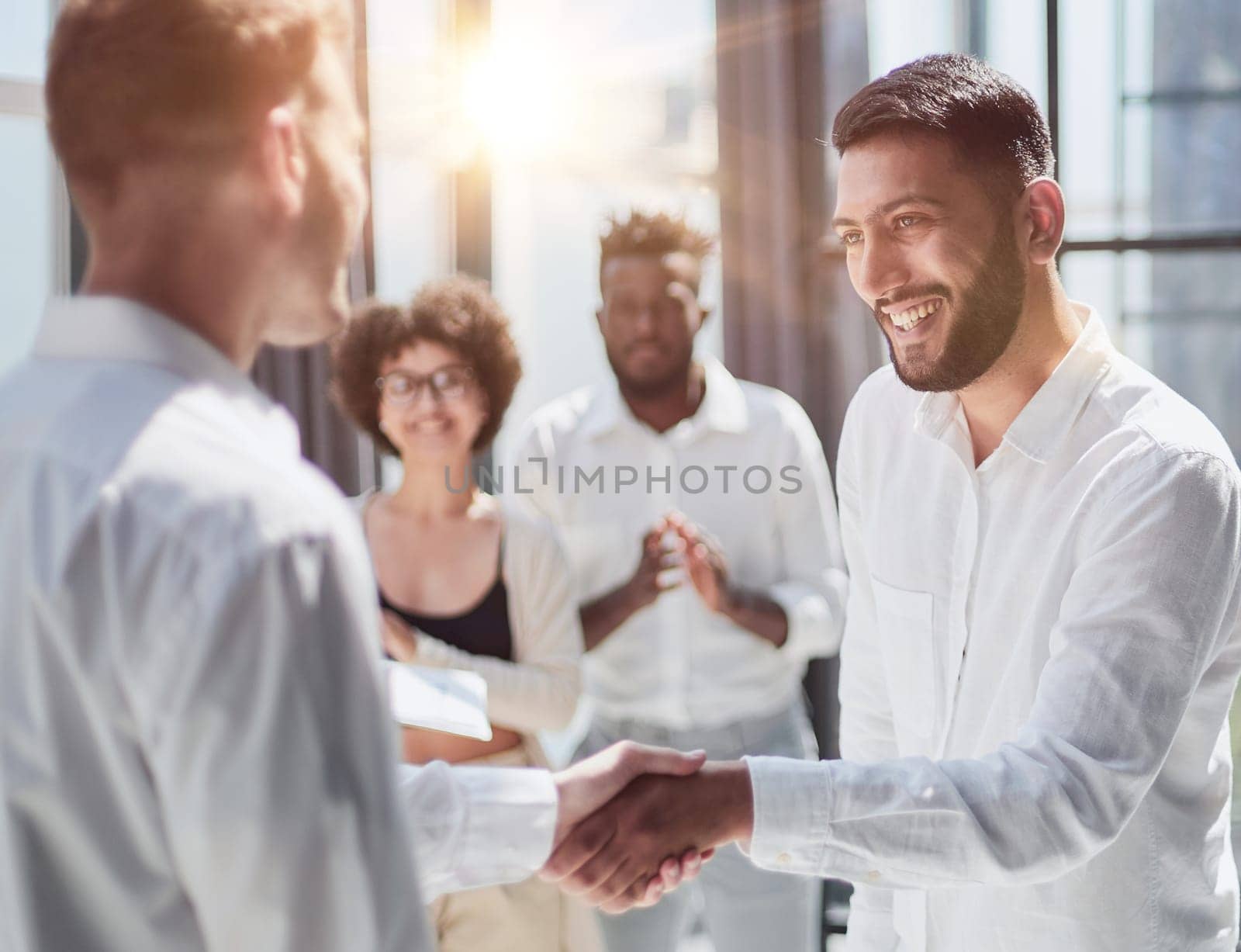 Glad to work with you. Young modern men in smart casual wear shaking hands and smiling while working in the creative office