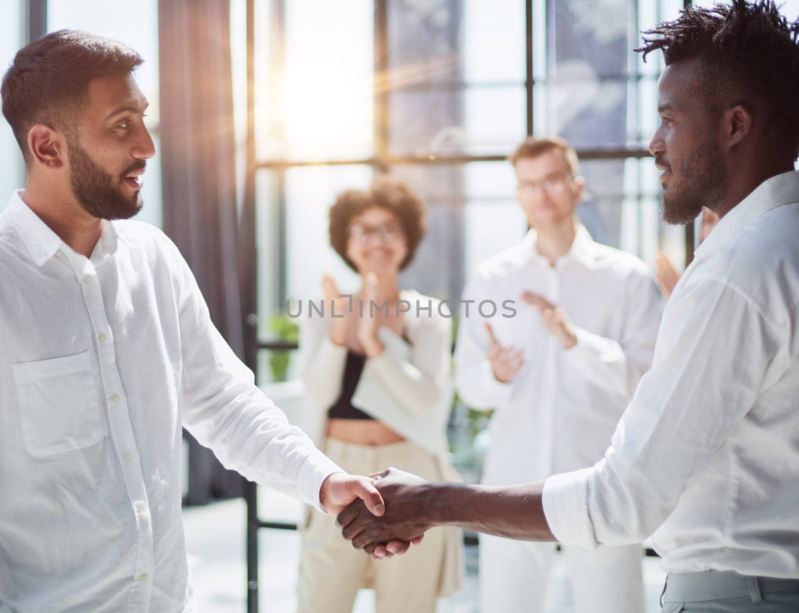 Glad to work with you. Young modern men in smart casual wear shaking hands and smiling while working in the creative office