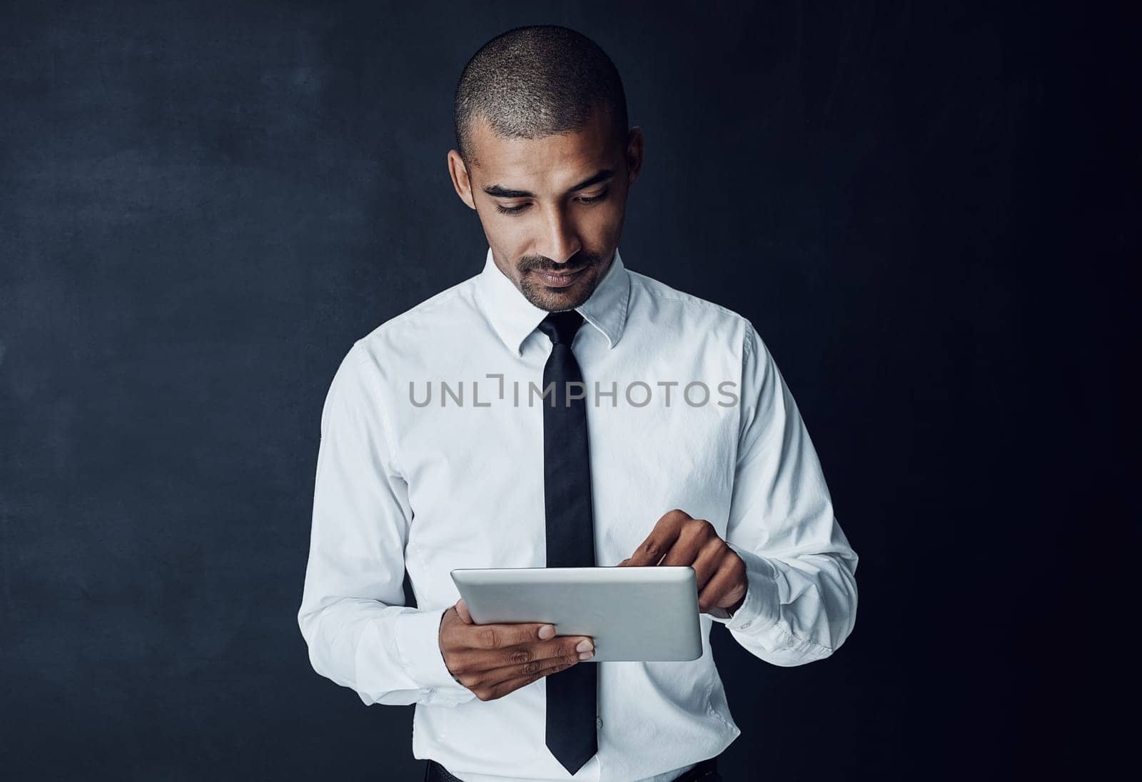 Business dealings done digitally. Studio shot of a young businessman using a digital tablet against a dark background