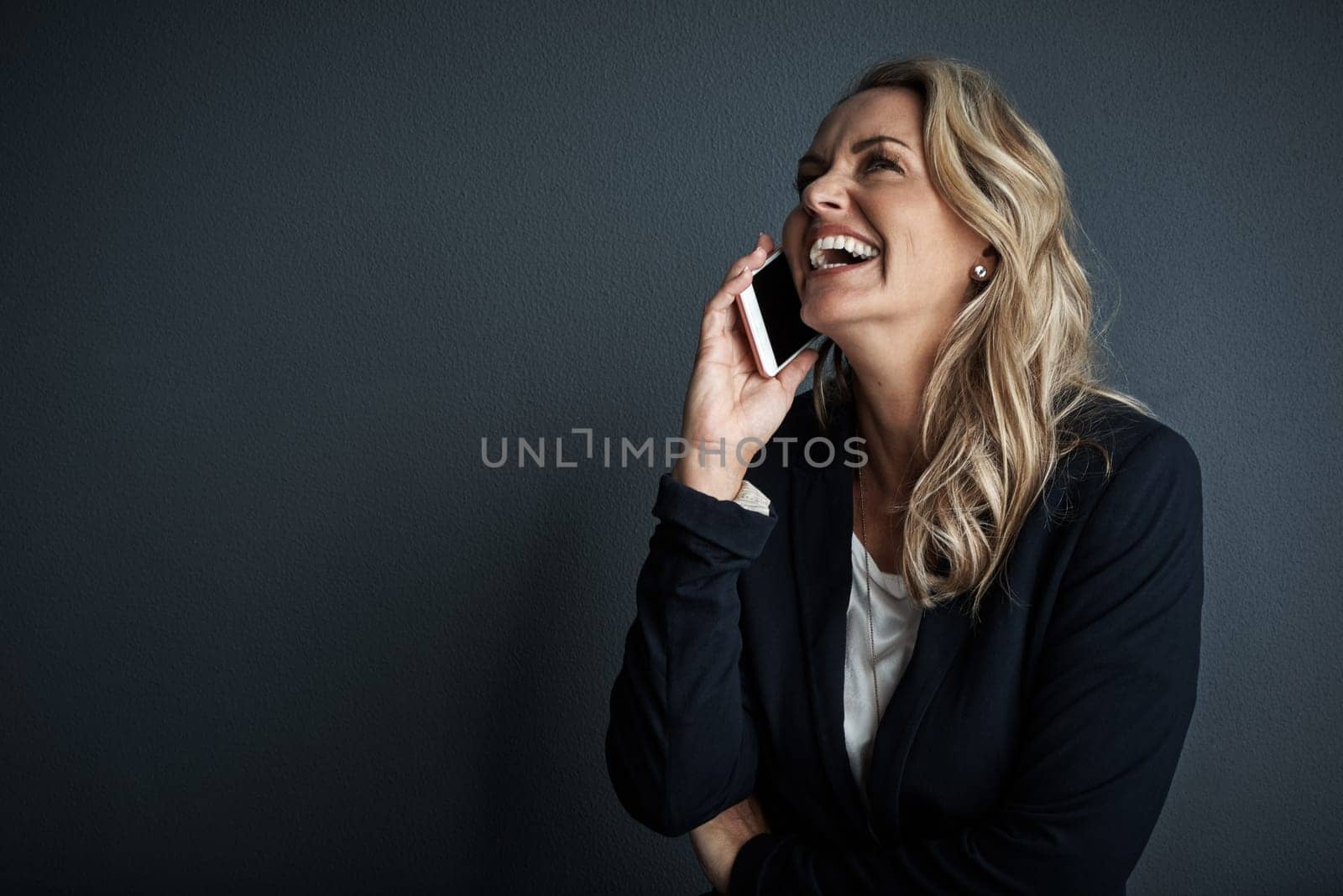 Sounds like shes made another success. Studio shot of a mature businesswoman talking on a cellphone against a grey background. by YuriArcurs