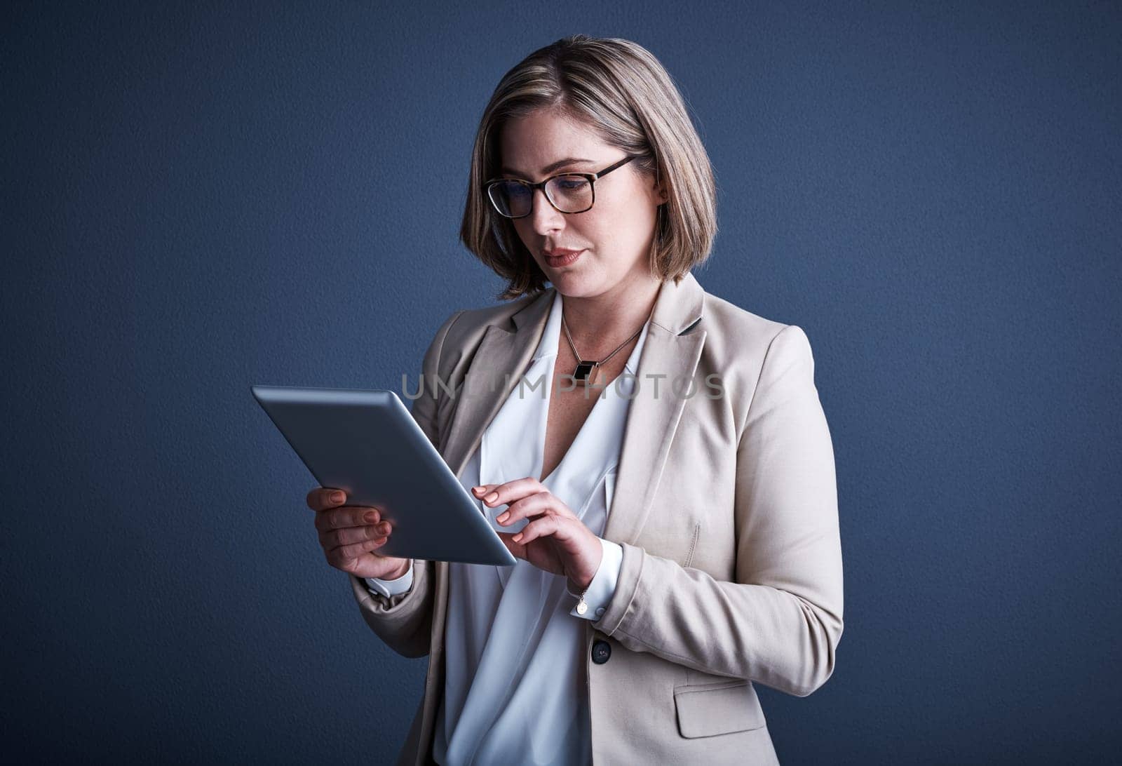 Sifting through the information. Studio shot of an attractive young corporate businesswoman using a tablet against a dark background. by YuriArcurs