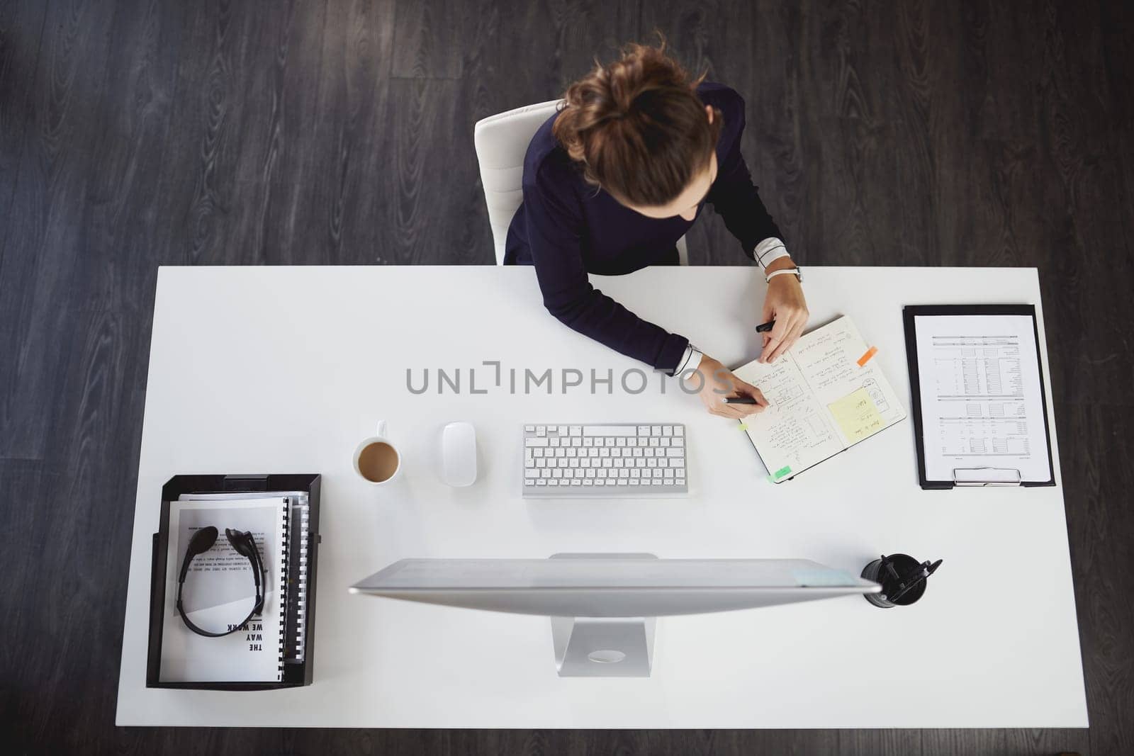 Ive got it all planned out. Aerial shot of an unrecognizable young businesswoman sitting at her desk and writing notes in a modern office. by YuriArcurs