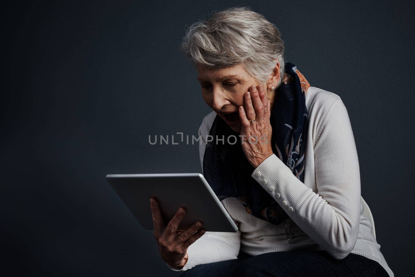 This contraption is wonderful. Studio shot of an cheerful elderly woman standing and using a tablet. by YuriArcurs