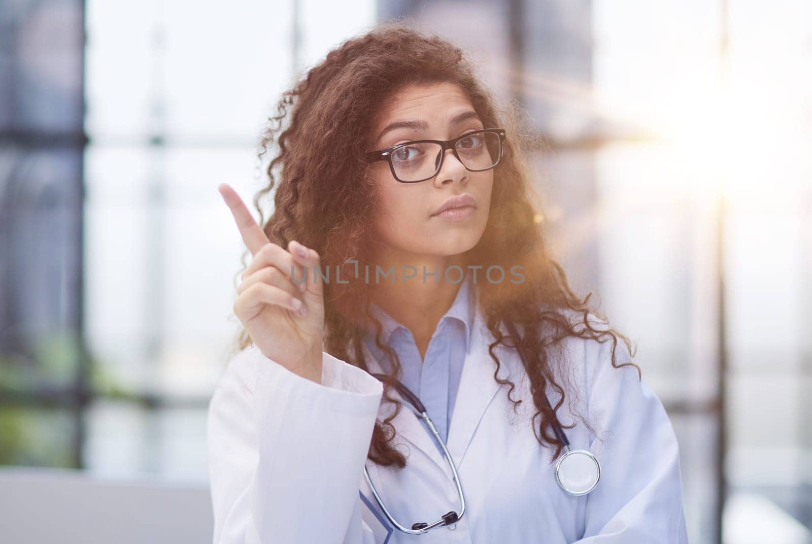 Portrait of an attractive young female doctor in a white coat points her finger
