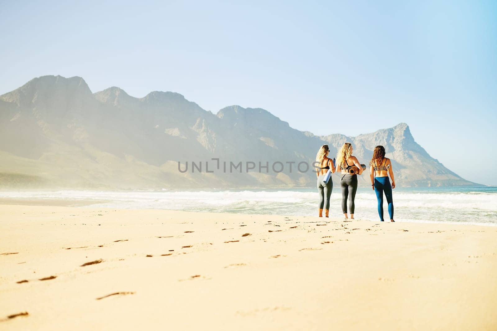 Yoga helps you maintain, recover or improve your health. Rearview shot of three young woman looking for a spot on the beach to practice yoga