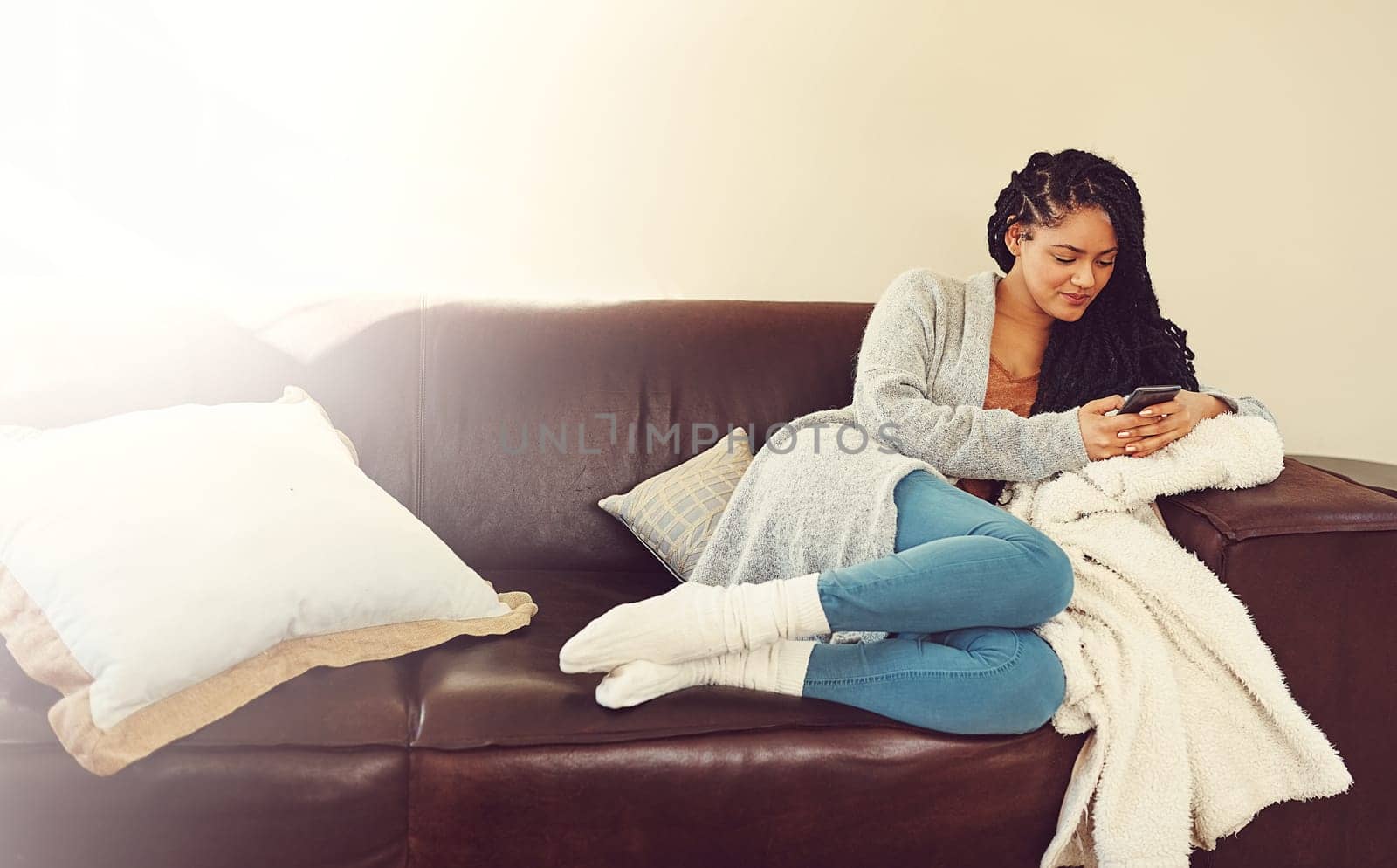 I cant wait for him to come over. a young woman using her phone while relaxing in her her living room