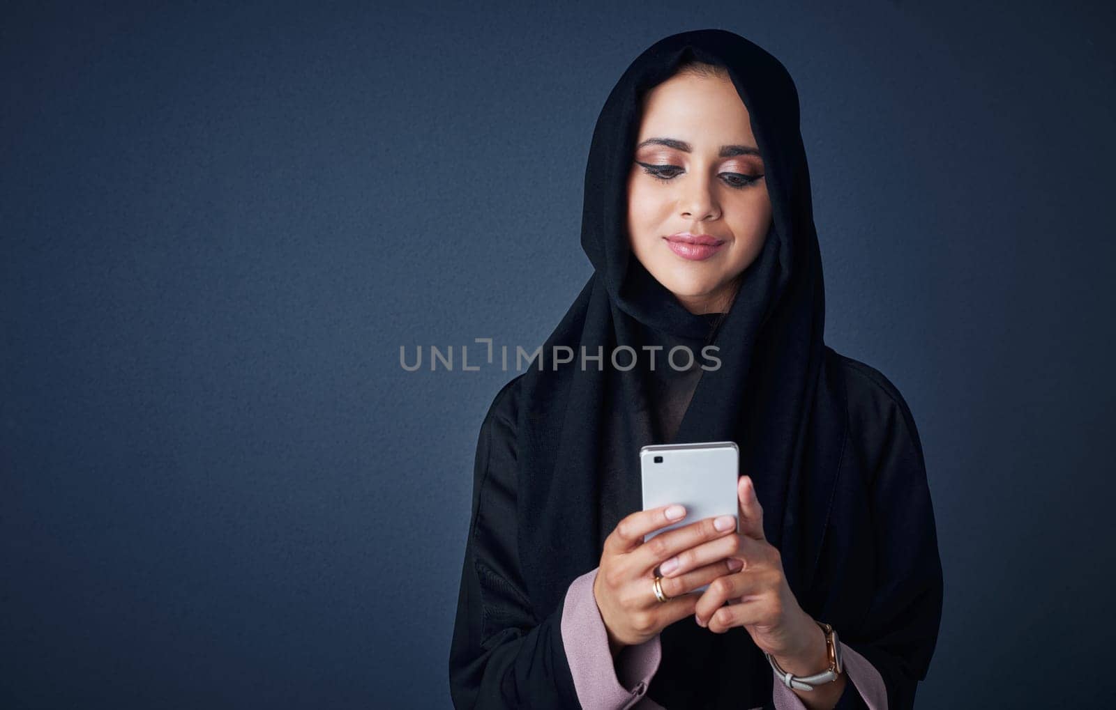 Keeping her lifestyle mobile. Studio shot of a young woman wearing a burqa and using a mobile phone against a gray background. by YuriArcurs