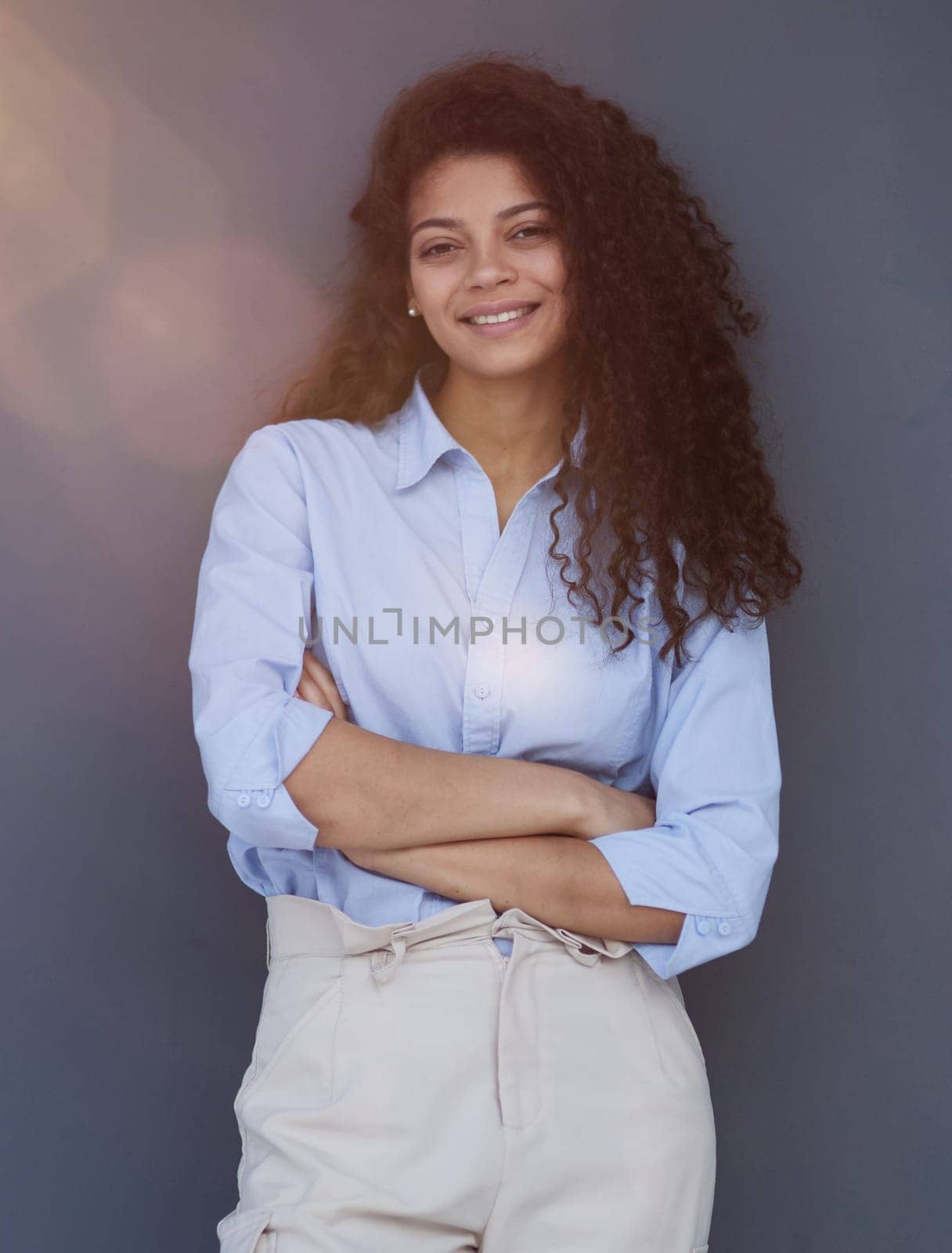 Smiling attractive young business woman in blue shirt posing on gray background by Prosto