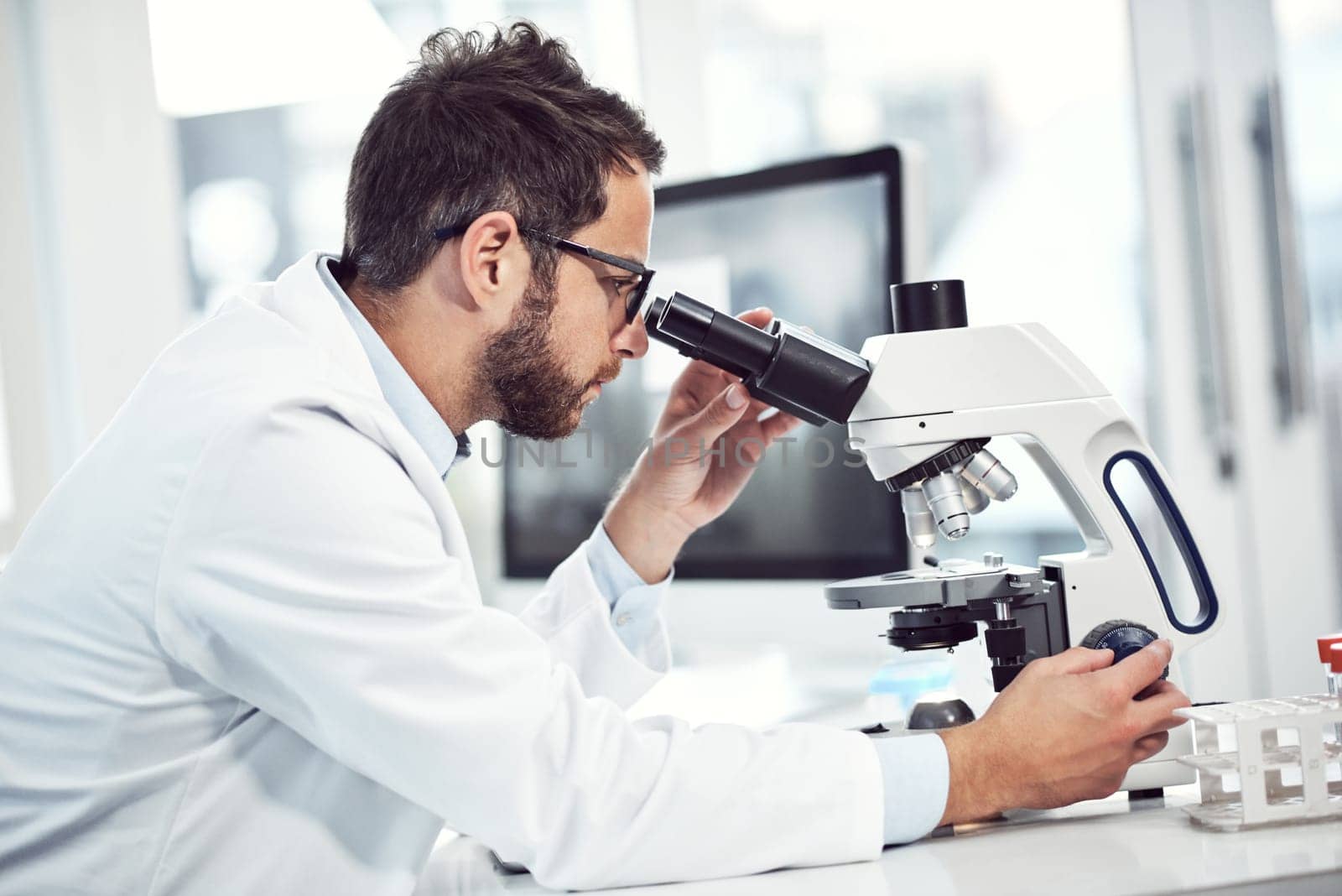 This part requires a lot of focus. a focused young male scientist looking through a microscope while being seated inside of a laboratory