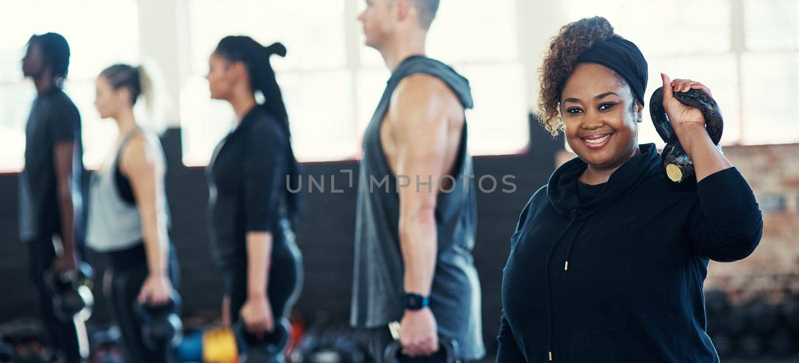 All about that fitness. a cheerful group of young people standing in a row and training with weights while one looks into the camera in a gym. by YuriArcurs