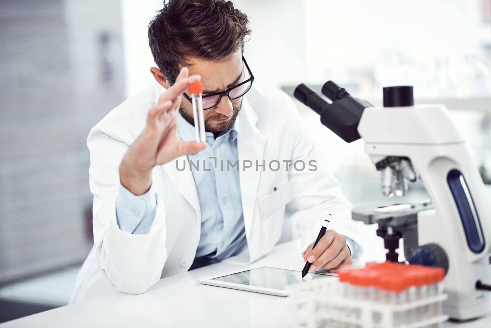 I have to make a record of this. a focused young male scientist making notes while holding up a test tube inside of a laboratory. by YuriArcurs
