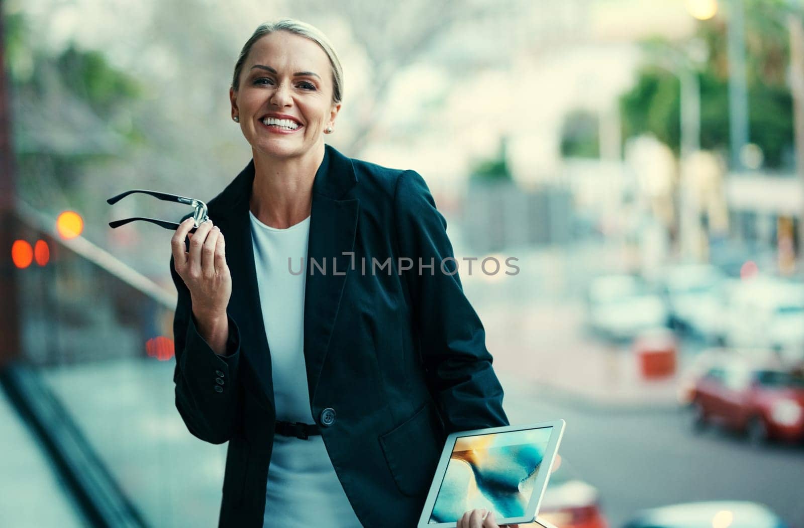 Its hard not to be happy when youre successful. Portrait of a mature businesswoman standing outside on the balcony of an office and holding a digital tablet. by YuriArcurs