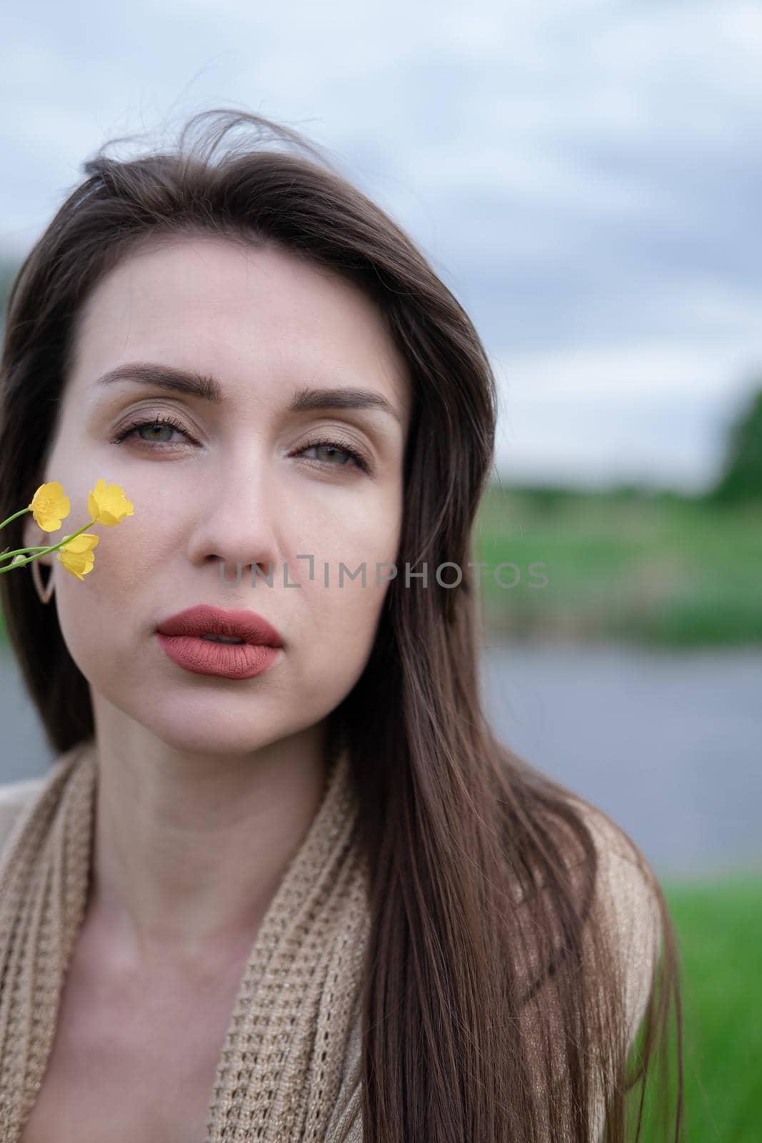 portrait of beautiful brunette woman with yellow small wildflower. skin care, nature.