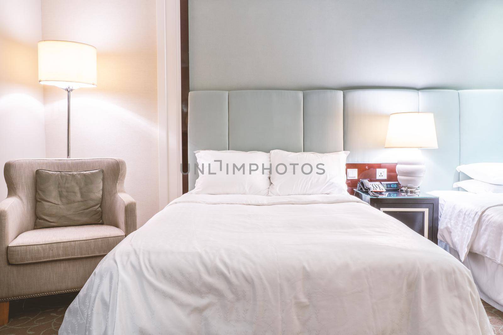 Clean and cozy modern hotel bedroom interior, warm tone room with a standing lamp, linen sofa with a cushion, design concept of luxury travel, close up.