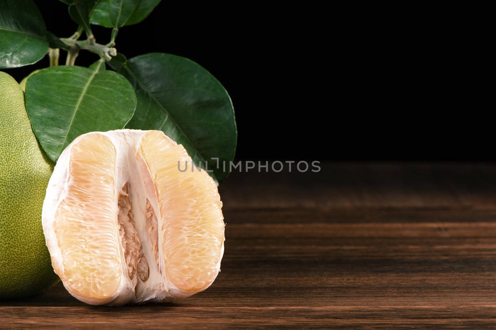 Fresh peeled pomelo, grapefruit, shaddock with green leaves on dark wooden plank table. Seasonal fruit near mid-autumn festival, close up, copy space