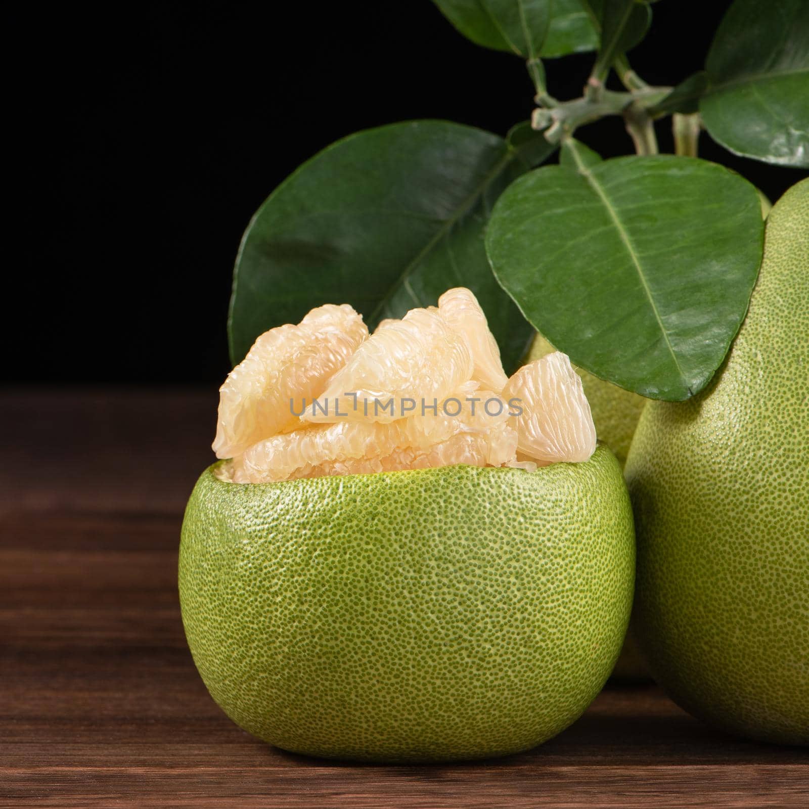 Fresh peeled pomelo, grapefruit, shaddock with green leaves on dark wooden plank table. Seasonal fruit near mid-autumn festival, close up, copy space by ROMIXIMAGE