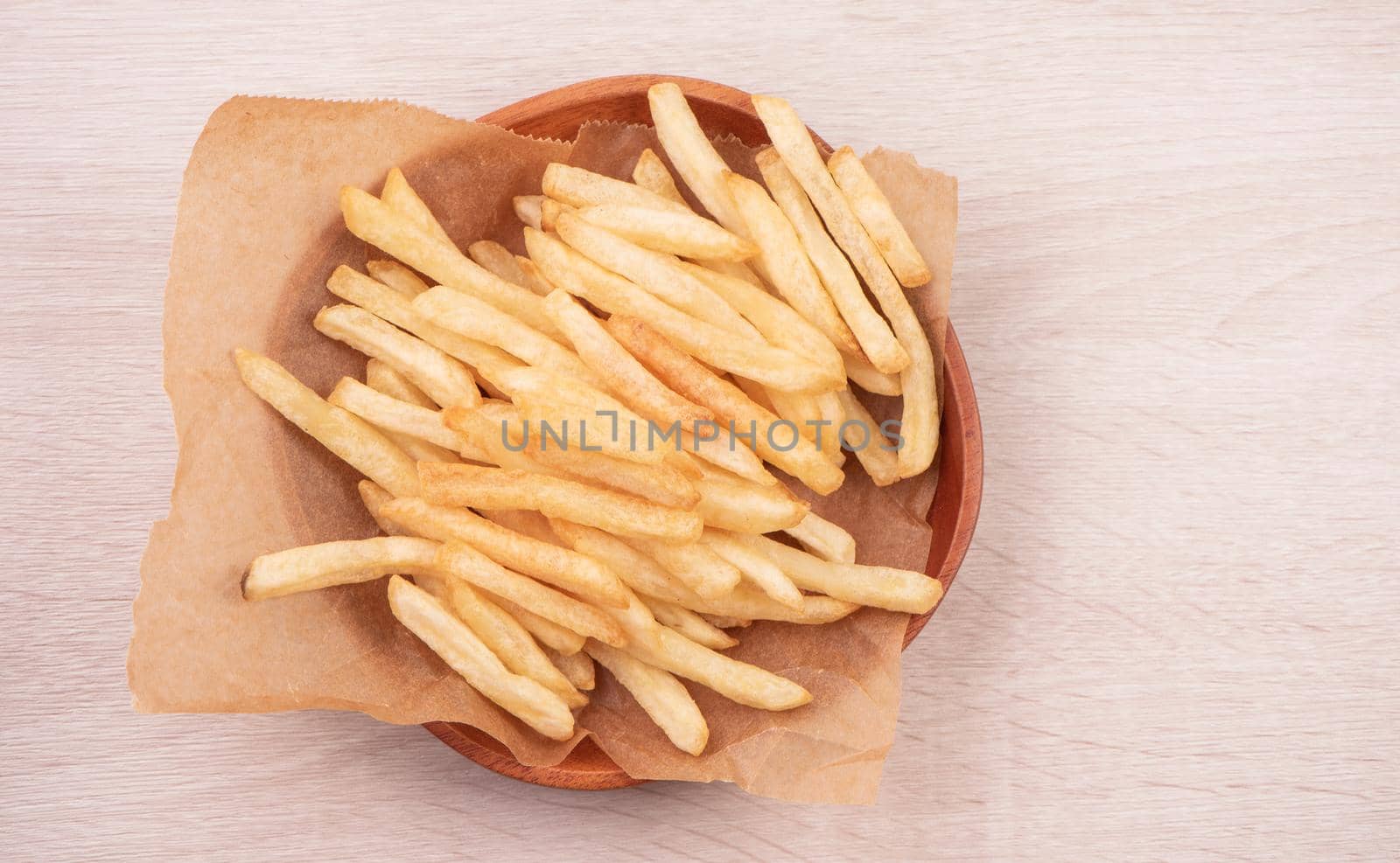 Golden yummy deep French fries on kraft baking sheet paper and serving tray to eat with ketchup and yellow mustard, top view, lifestyle.