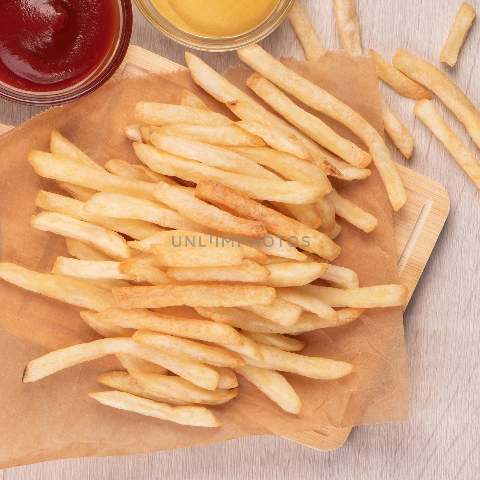 Golden yummy deep French fries on kraft baking sheet paper and serving tray to eat with ketchup and yellow mustard, top view, lifestyle. by ROMIXIMAGE