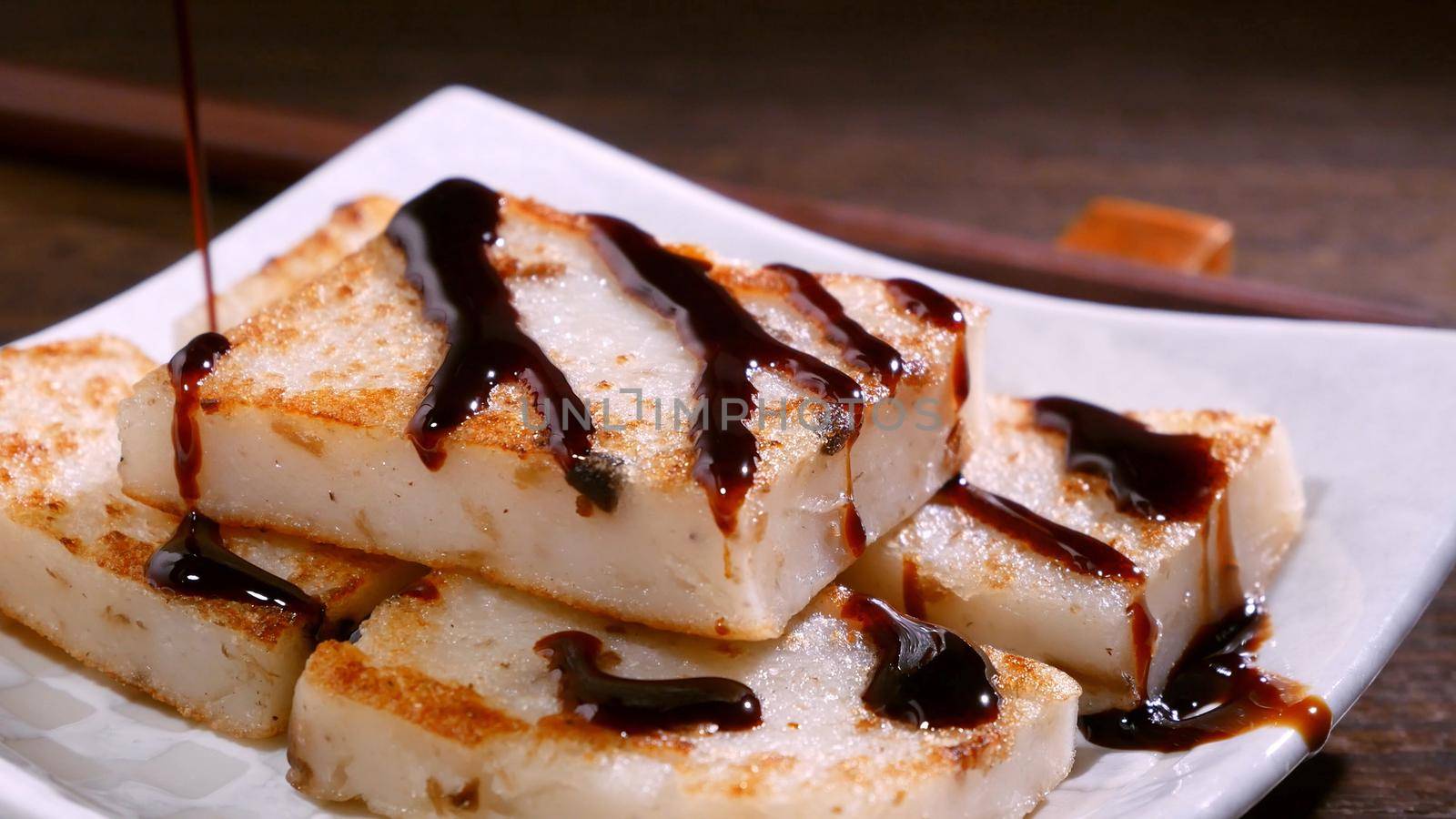 Pouring black soy sauce on ready-to-eat delicious turnip cake, Chinese traditional local dish radish cake in restaurant, close up, copy space.