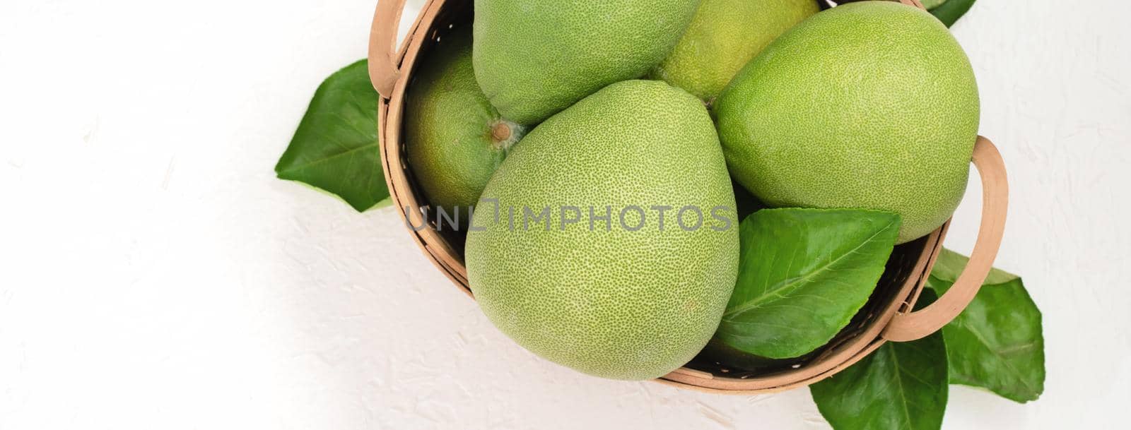 Fresh pomelo, pummelo, grapefruit, shaddock on white cement background in bamboo basket. Autumn seasonal fruit, top view, flat lay, tabletop shot.