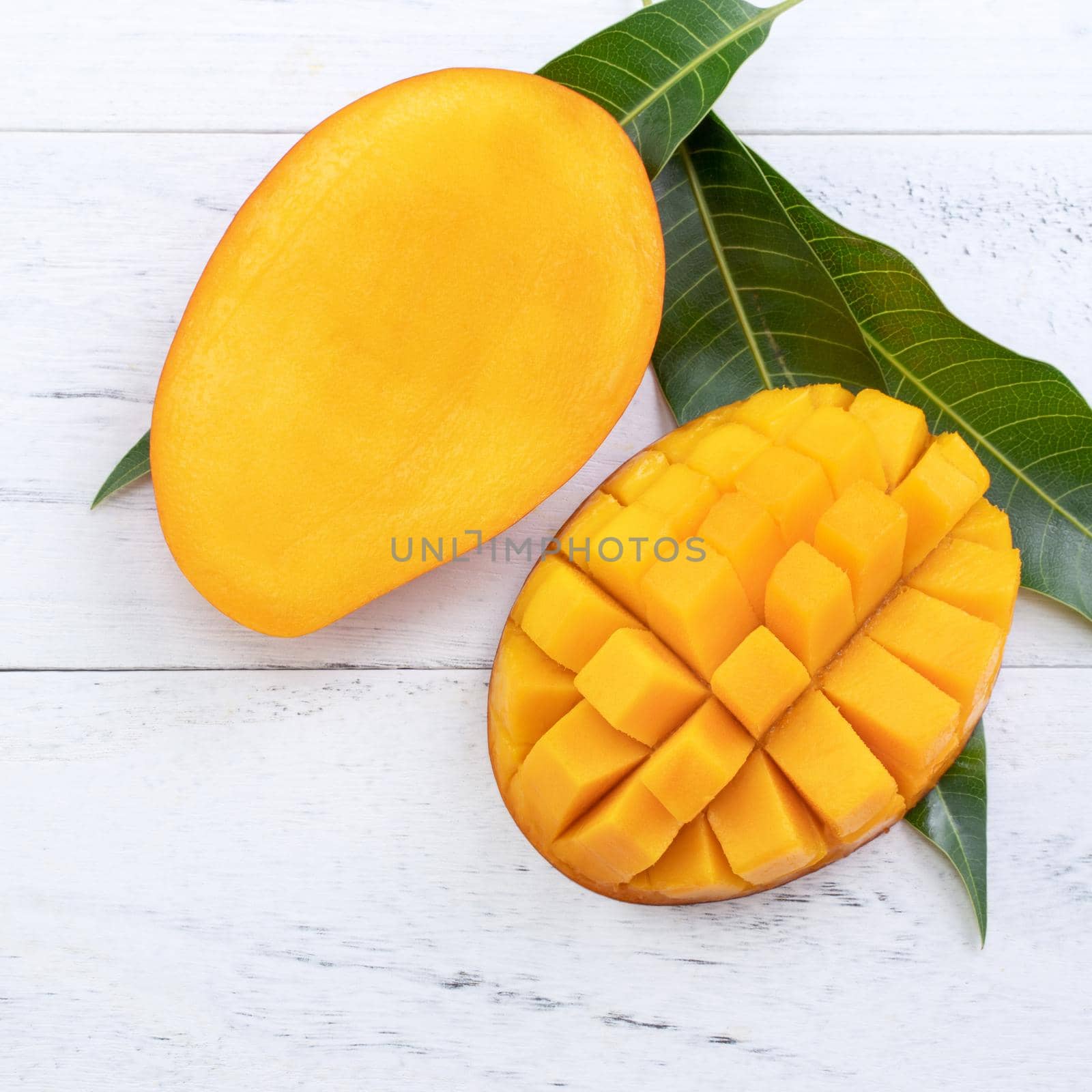 Beautiful chopped ripe mango with green leaves on bright white color wooden background, top view, flat lay, copy space. Tropical fruit design concept. by ROMIXIMAGE