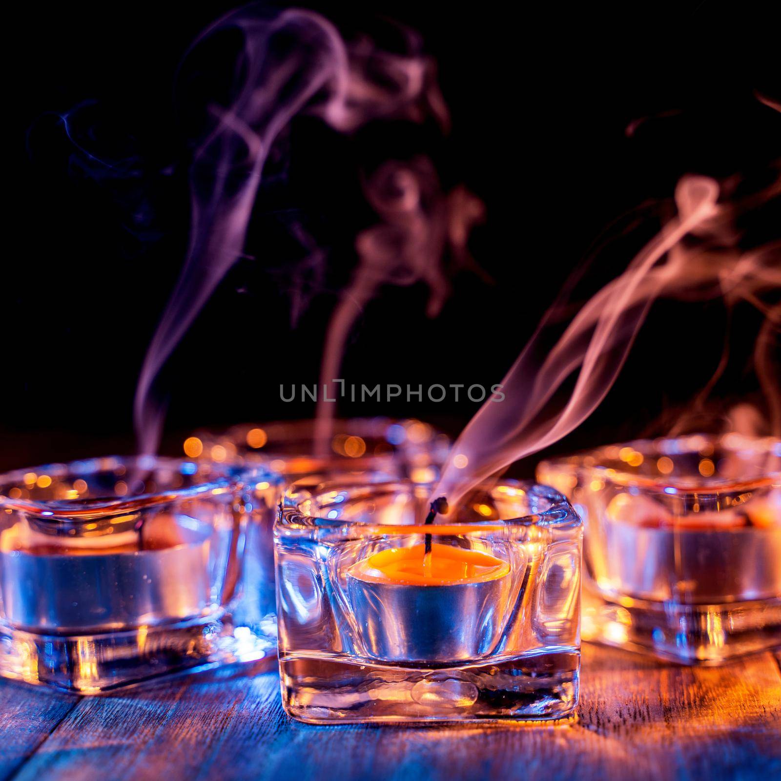 Halloween concept, spooky decorations with lighting up candle and candle holder with blue tone smoke around on a dark wooden table, close up.