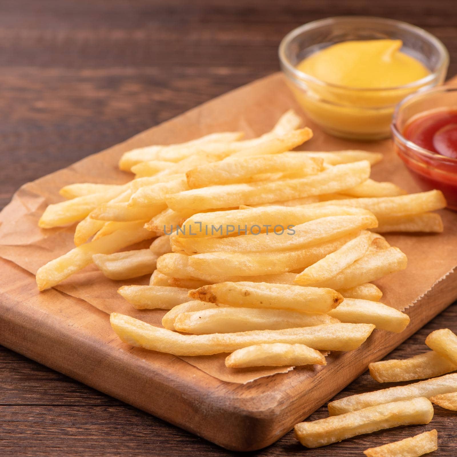Golden yummy deep French fries on kraft baking sheet paper and serving tray to eat with ketchup and yellow mustard, top view, lifestyle.