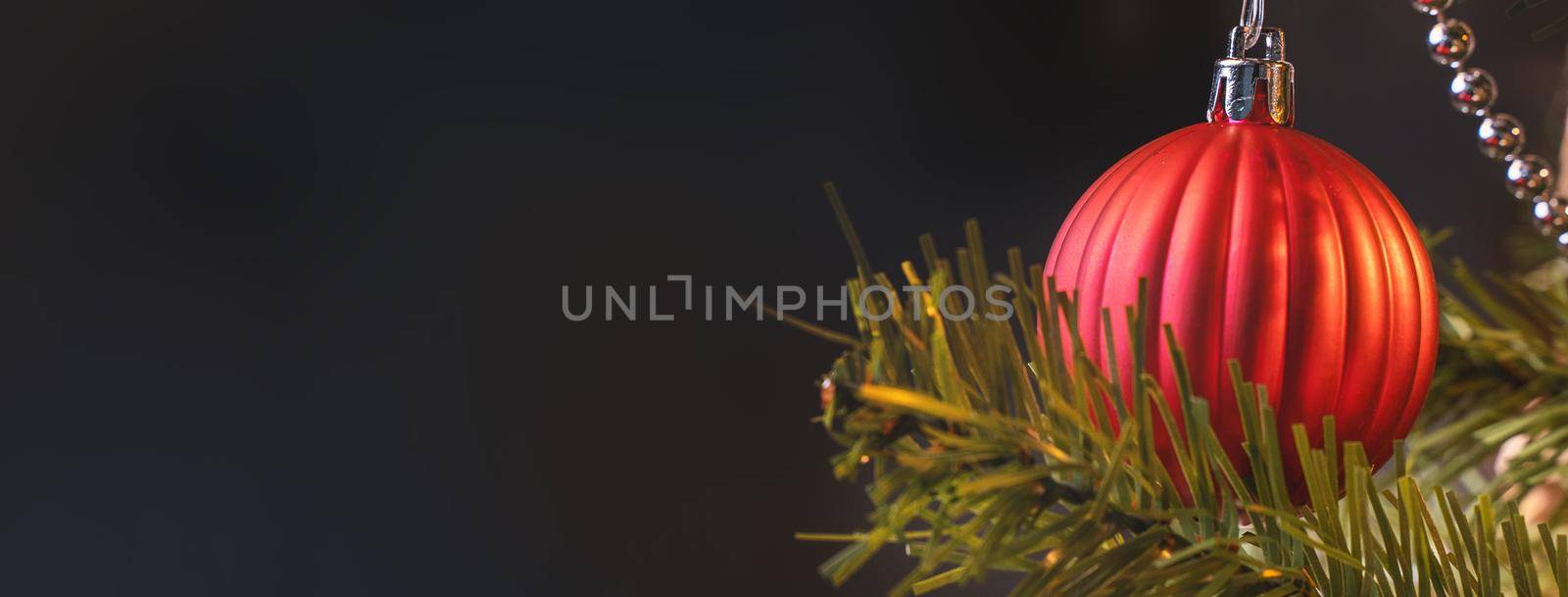 Beautiful Christmas decor concept, bauble hanging on the Christmas tree with sparkling light spot, blurry dark black background, macro detail, close up.