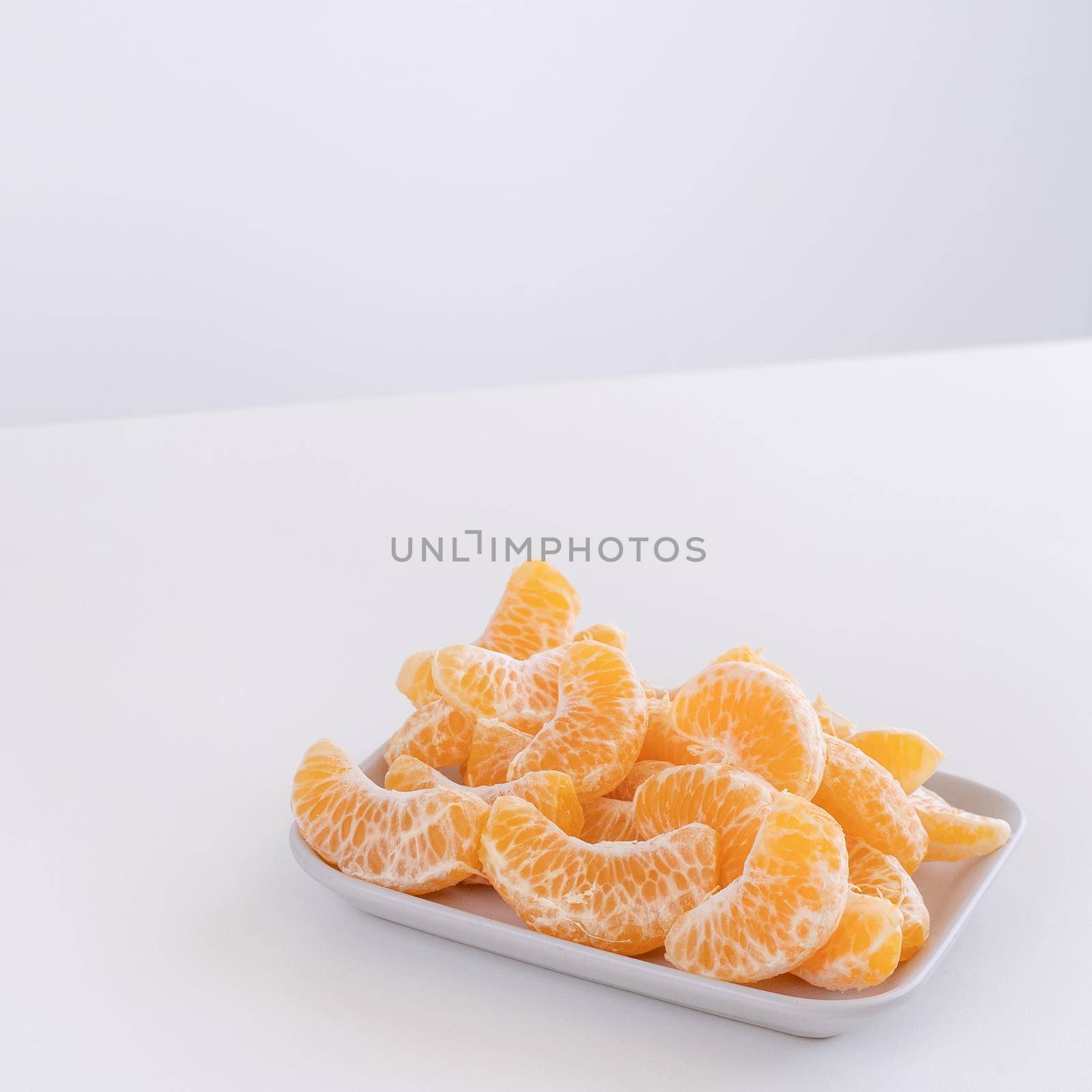 Beautiful peeled tangerines in a plate and metal basket isolated on bright white clean table in a modern contemporary kitchen island, close up.