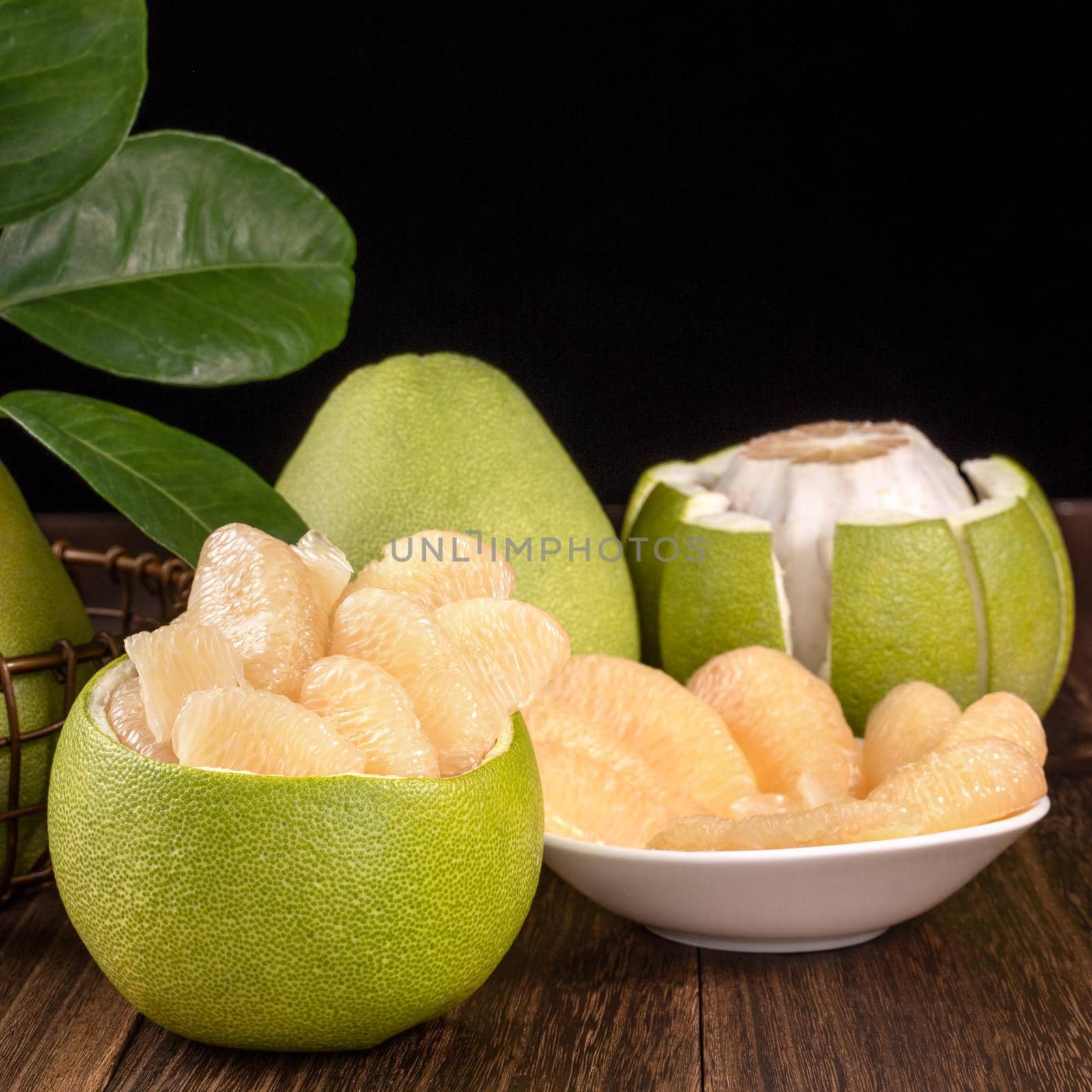 Fresh peeled pomelo, grapefruit, shaddock with green leaves on dark wooden plank table. Seasonal fruit near mid-autumn festival, close up, copy space