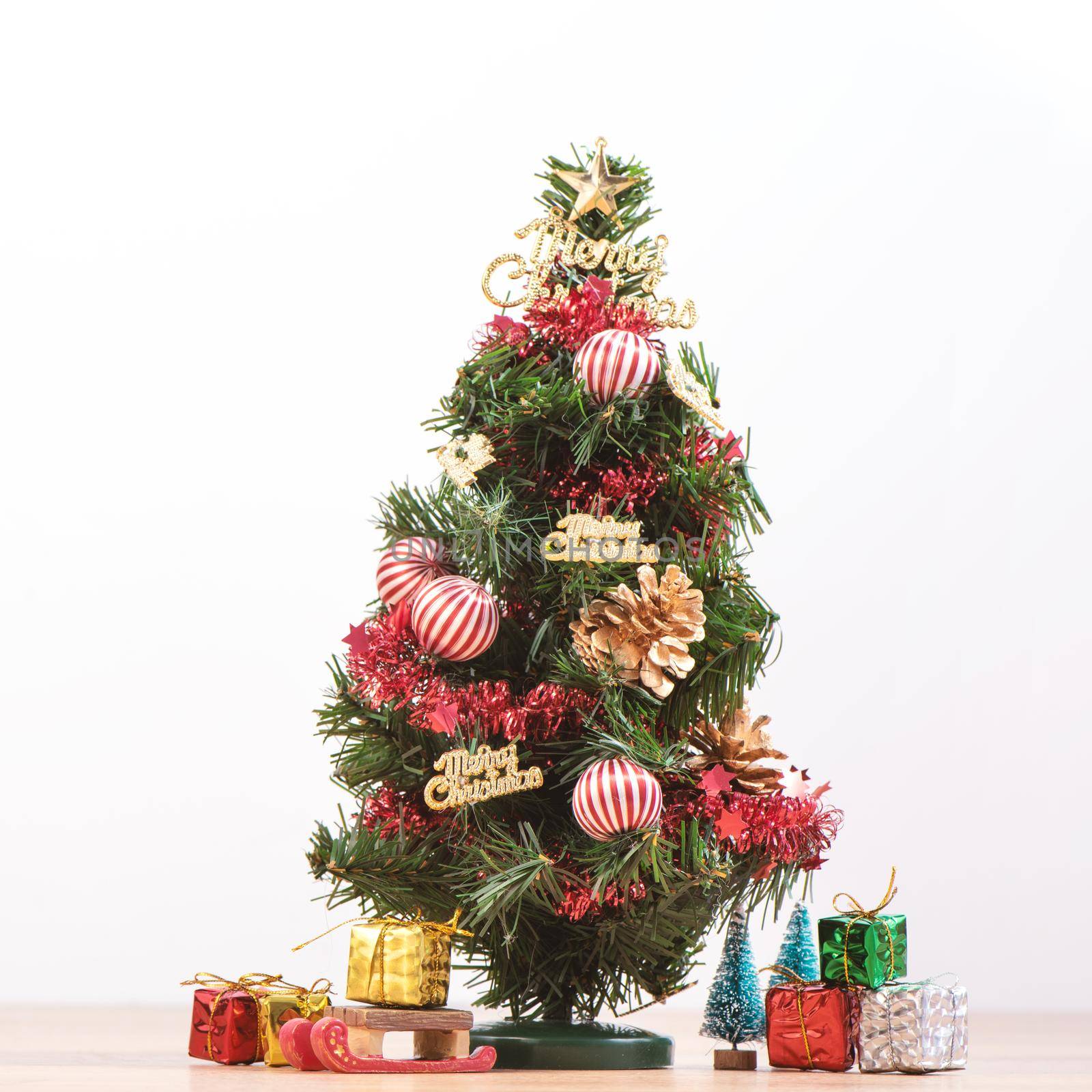 Decorated cute Christmas tree on a wooden floor with white background and toys, blank for festive design concept, close up.