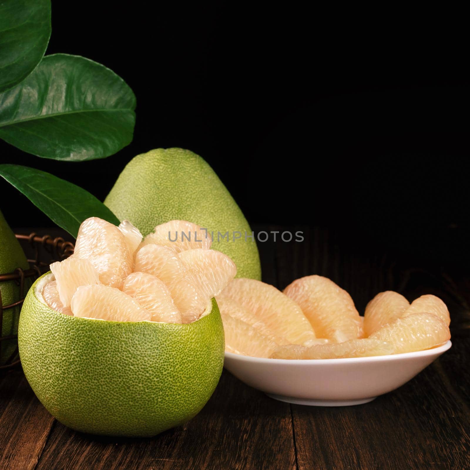 Fresh peeled pomelo, grapefruit, shaddock with green leaves on dark wooden plank table. Seasonal fruit near mid-autumn festival, close up, copy space