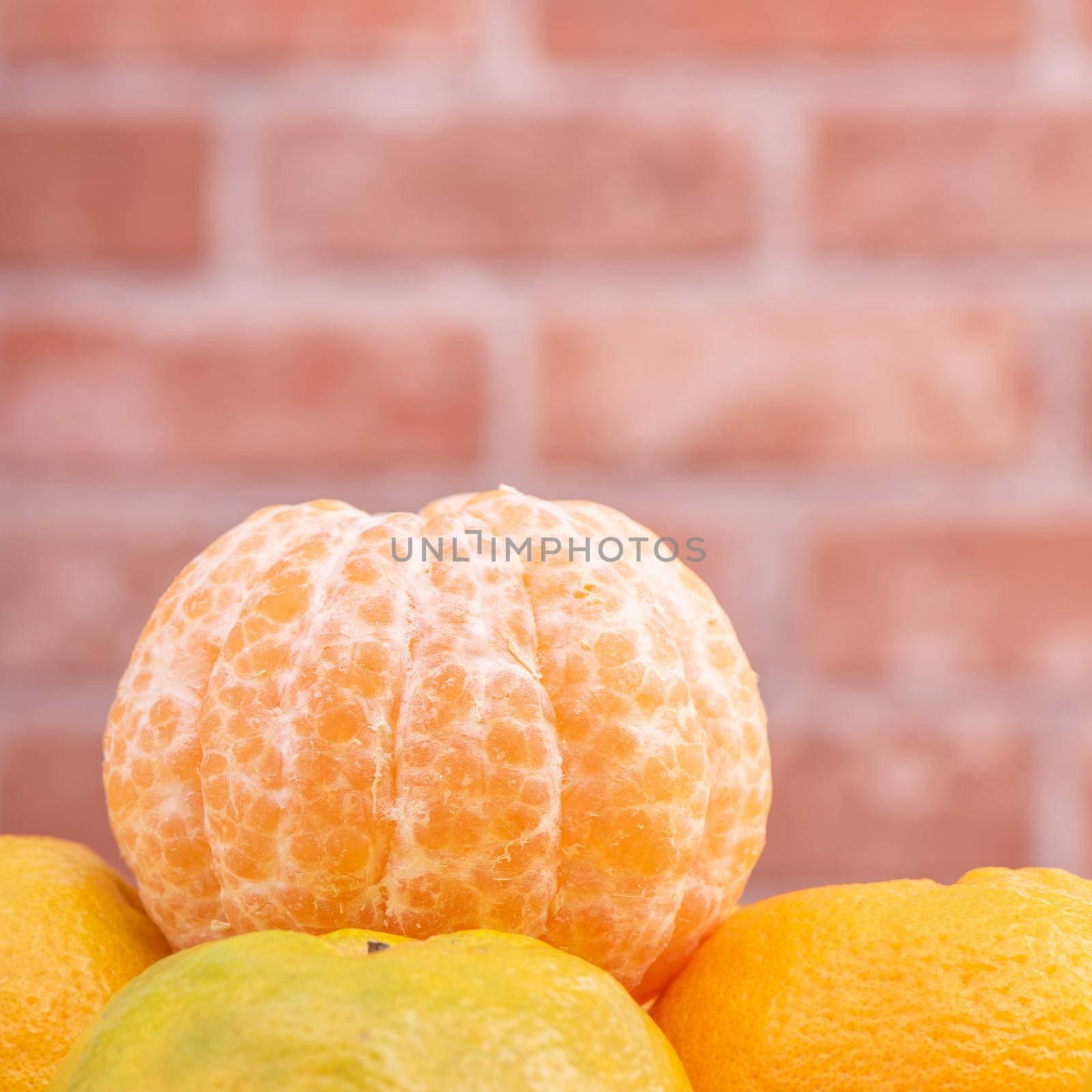 Peeled tangerines in a bamboo sieve basket on dark wooden table with red brick wall background, Chinese lunar new year fruit design concept, close up.