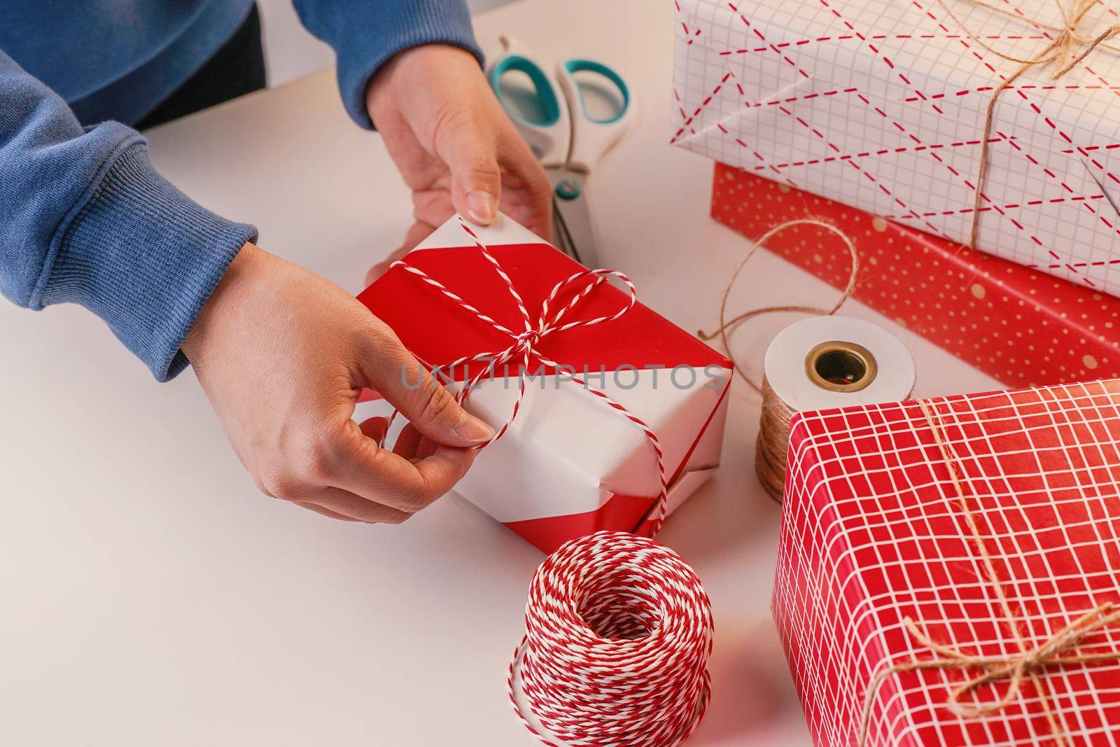 A young woman in blue is wrapping, packaging Christmas gift for kids children by beautiful, red, white wrapper with glittering light, lifestyle.