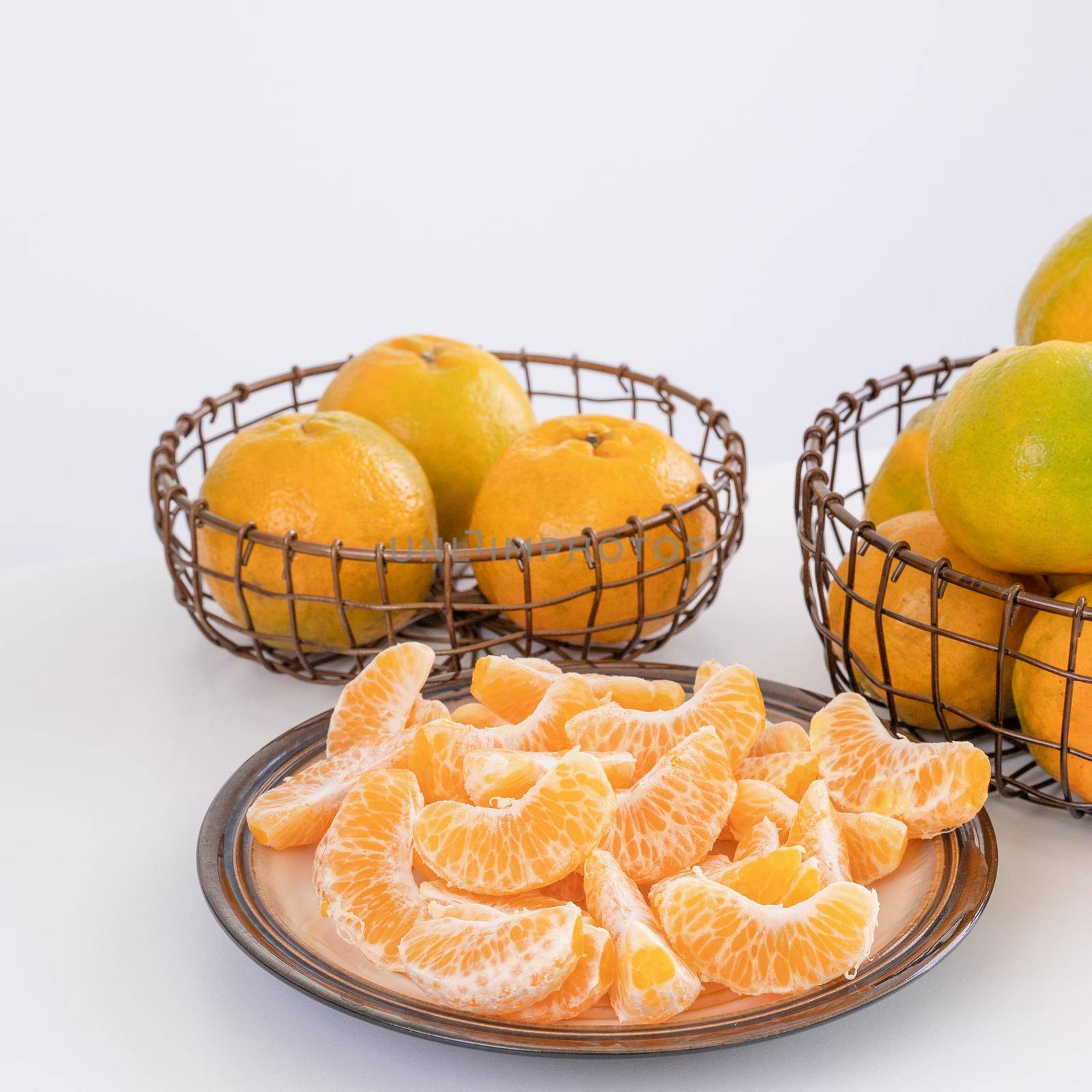 Beautiful peeled tangerines in a plate and metal basket isolated on bright white clean table in a modern contemporary kitchen island, close up. by ROMIXIMAGE