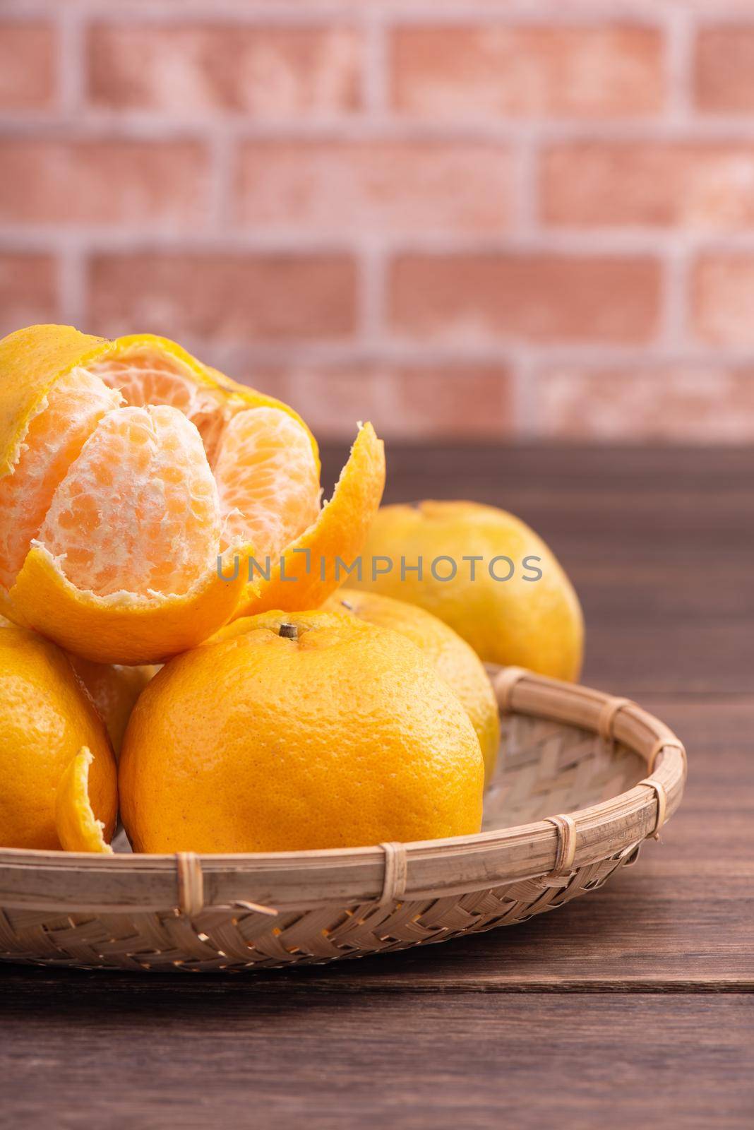 Peeled tangerines in a bamboo sieve basket on dark wooden table with red brick wall background, Chinese lunar new year fruit design concept, close up.