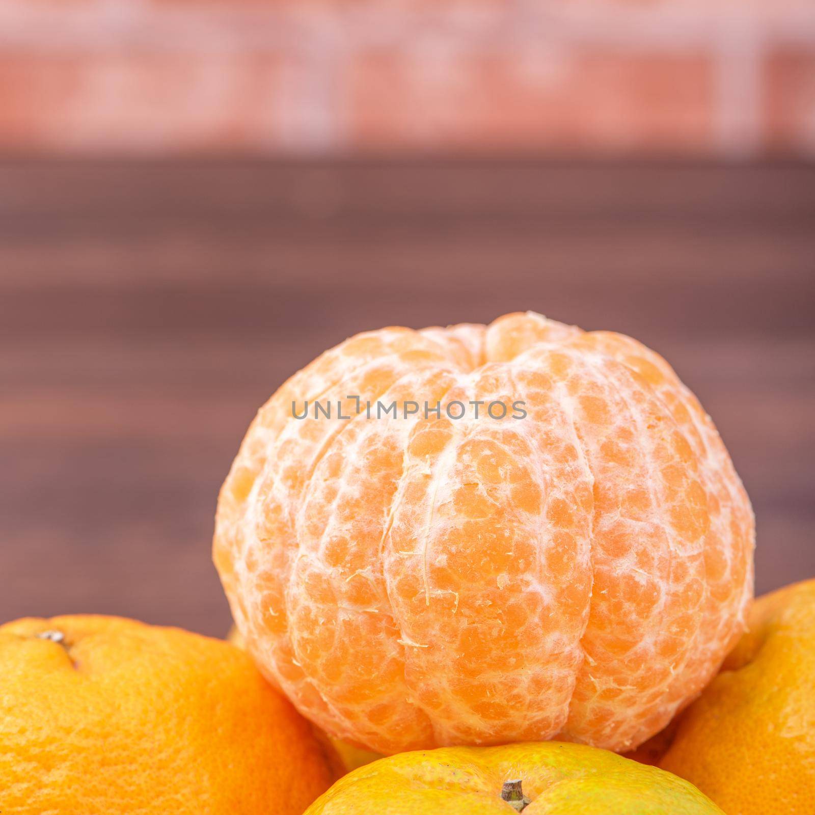 Peeled tangerines in a bamboo sieve basket on dark wooden table with red brick wall background, Chinese lunar new year fruit design concept, close up.