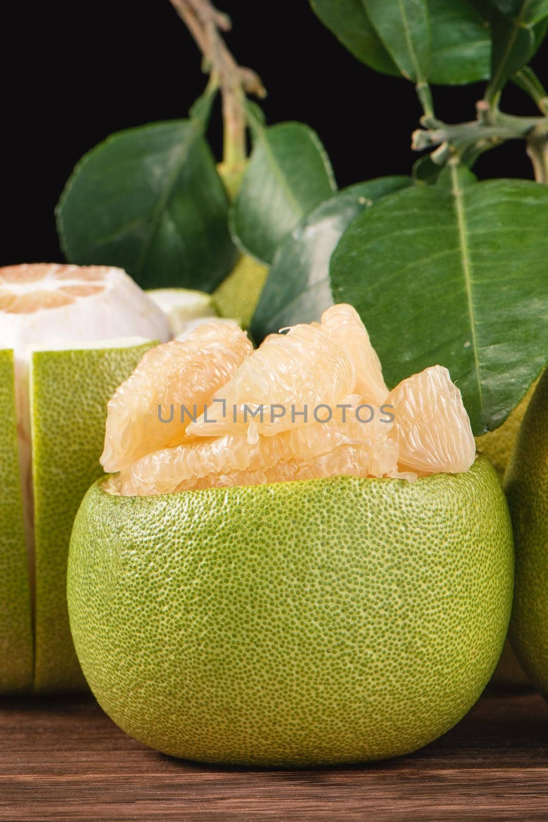 Fresh peeled pomelo, grapefruit, shaddock with green leaves on dark wooden plank table. Seasonal fruit near mid-autumn festival, close up, copy space by ROMIXIMAGE