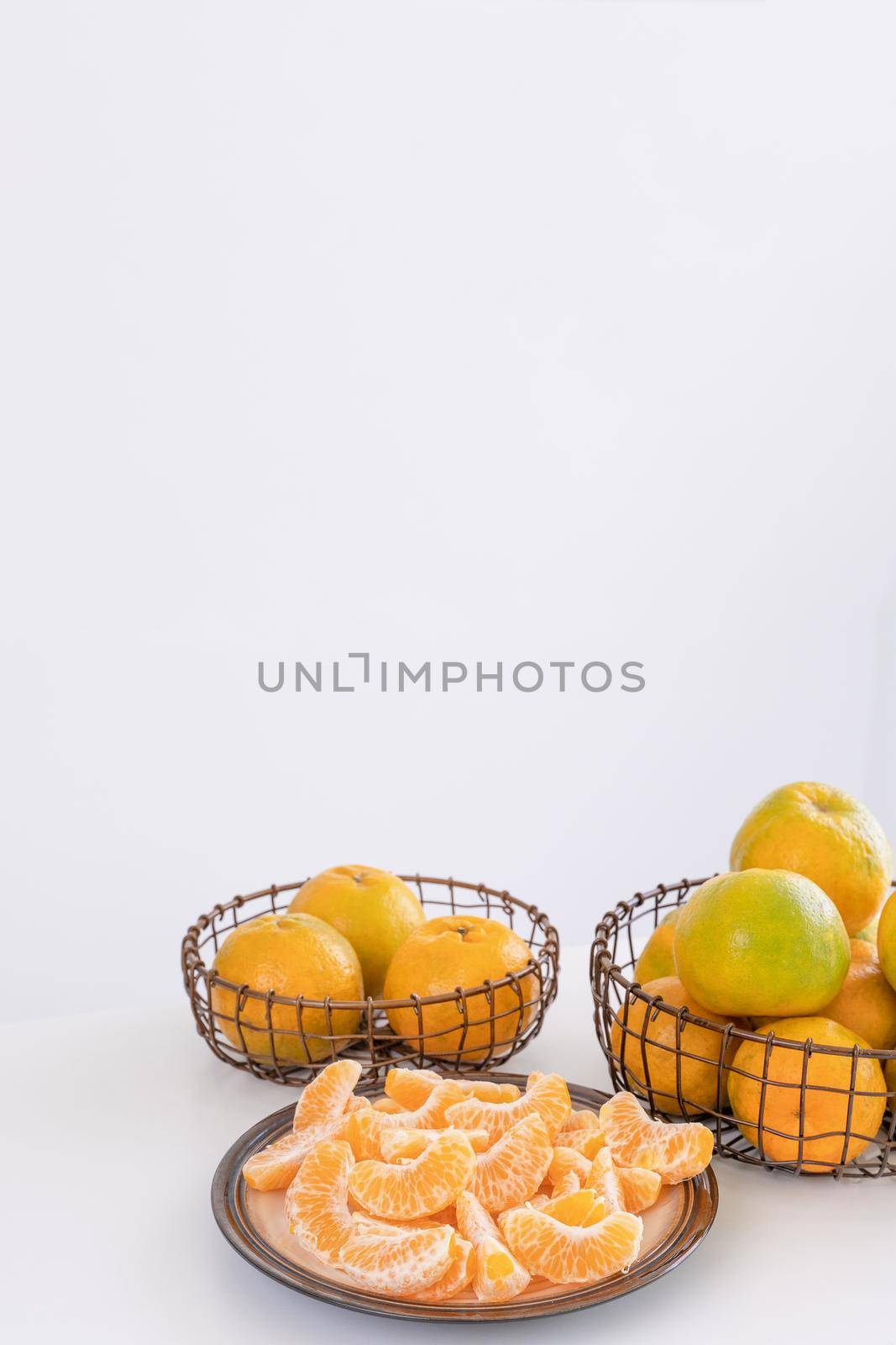 Beautiful peeled tangerines in a plate and metal basket isolated on bright white clean table in a modern contemporary kitchen island, close up. by ROMIXIMAGE