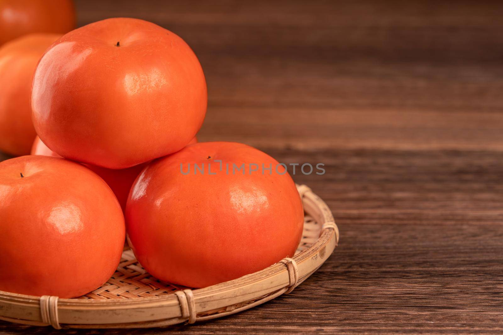 Sliced sweet persimmon kaki in a bamboo sieve basket on dark wooden table with red brick wall background, Chinese lunar new year fruit design concept, close up.