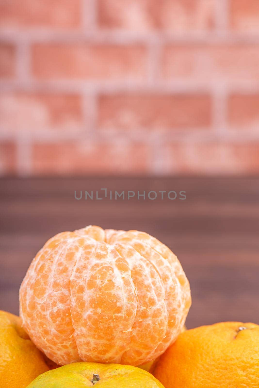 Peeled tangerines in a bamboo sieve basket on dark wooden table with red brick wall background, Chinese lunar new year fruit design concept, close up.