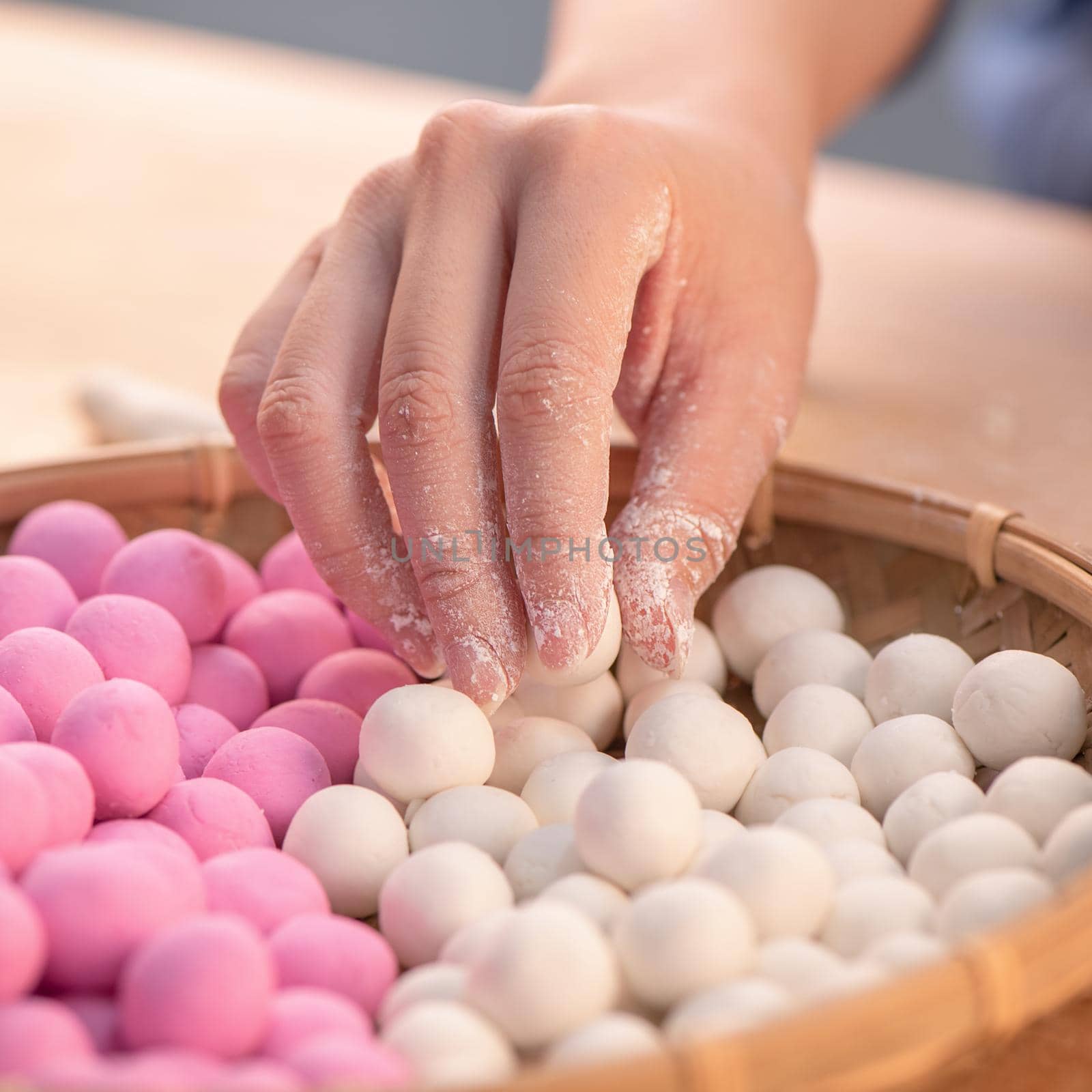 An Asia woman is making Tang yuan, yuan xiao, Chinese traditional food rice dumplings in red and white for lunar new year, winter festival, close up. by ROMIXIMAGE