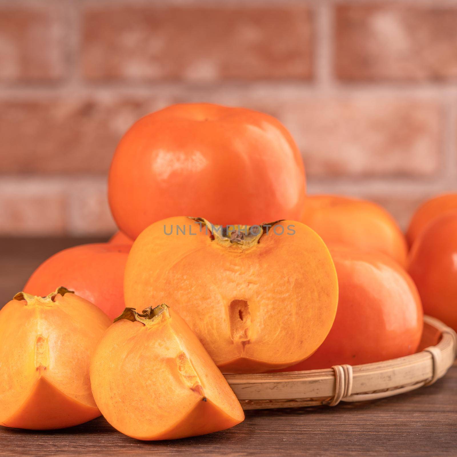 Fresh beautiful sliced sweet persimmon kaki on dark wooden table with red brick wall background, Chinese lunar new year fruit design concept, close up. by ROMIXIMAGE