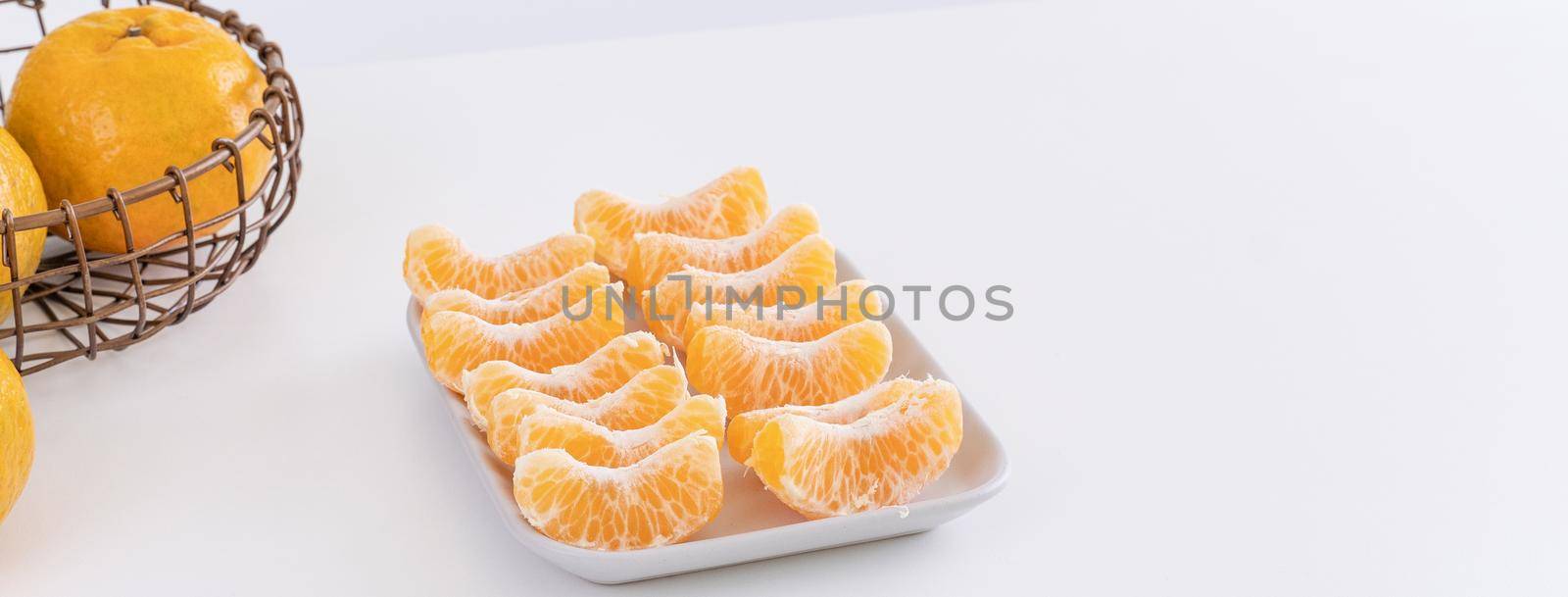 Beautiful peeled tangerines in a plate and metal basket isolated on bright white clean table in a modern contemporary kitchen island, close up.