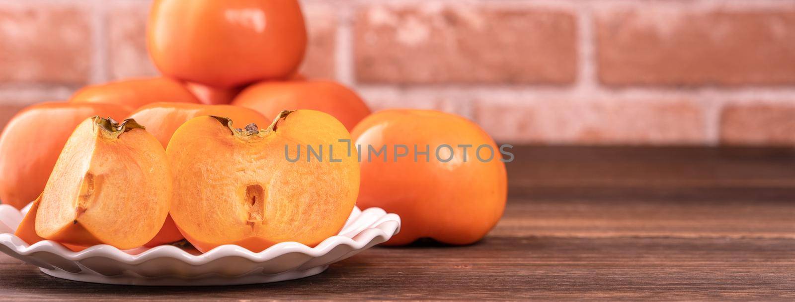 Sliced sweet persimmon kaki in a bamboo sieve basket on dark wooden table with red brick wall background, Chinese lunar new year fruit design concept, close up.