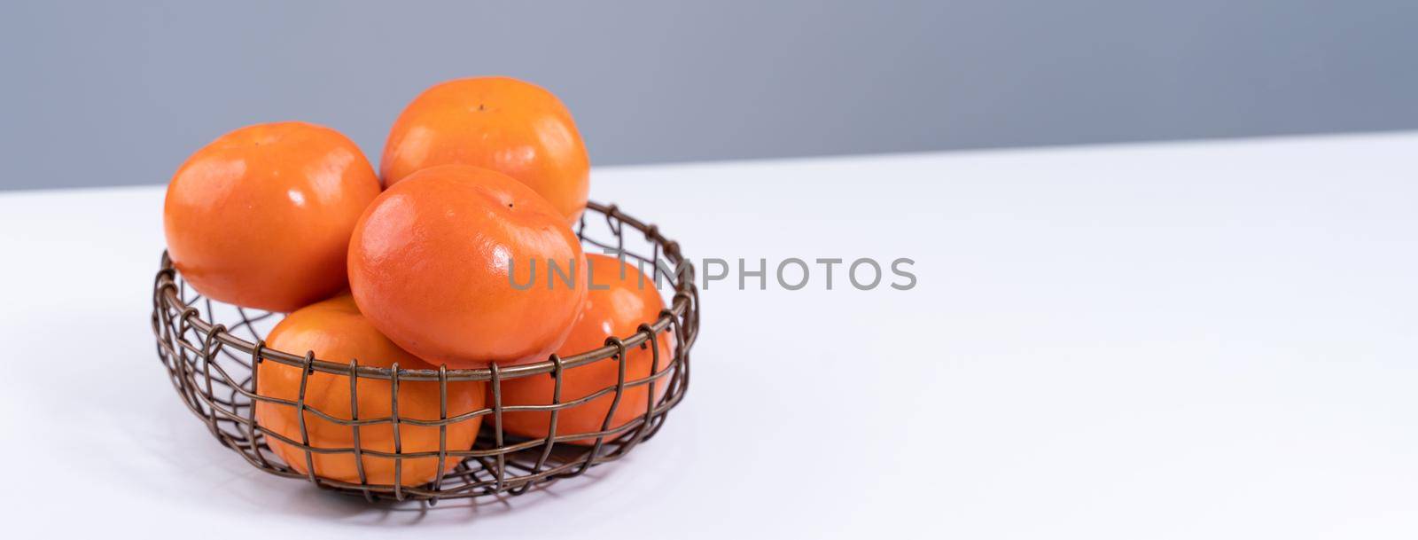 Fresh beautiful sliced sweet persimmon kaki isolated on white kitchen table with gray blue background, Chinese lunar new year design concept, close up. by ROMIXIMAGE