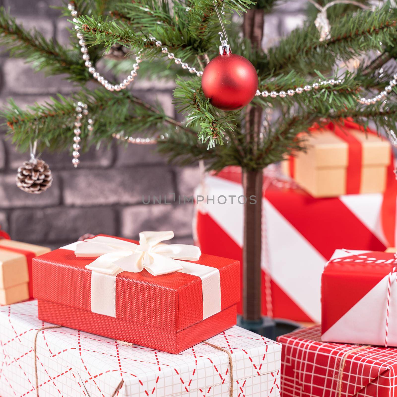 Decorated Christmas tree with wrapped beautiful red and white gifts at home with black brick wall, festive design concept, close up.