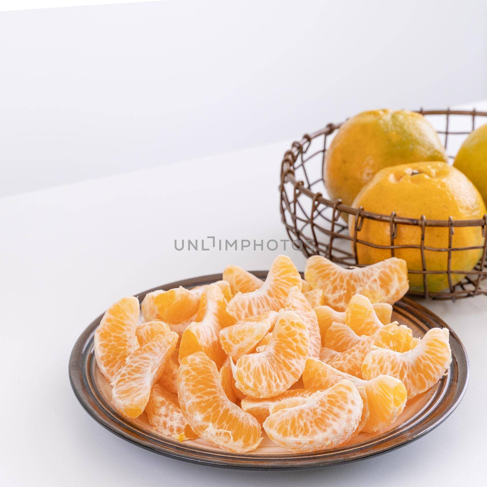 Beautiful peeled tangerines in a plate and metal basket isolated on bright white clean table in a modern contemporary kitchen island, close up.