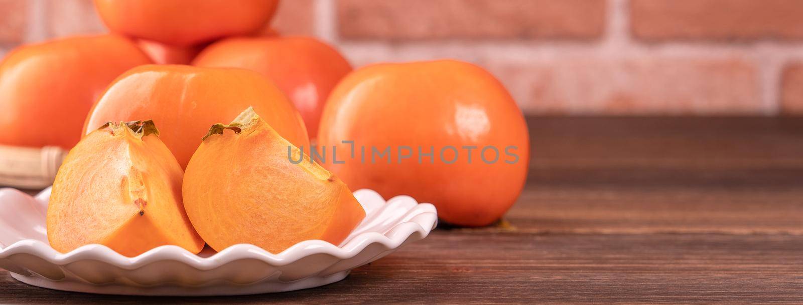 Fresh beautiful sliced sweet persimmon kaki on dark wooden table with red brick wall background, Chinese lunar new year fruit design concept, close up. by ROMIXIMAGE