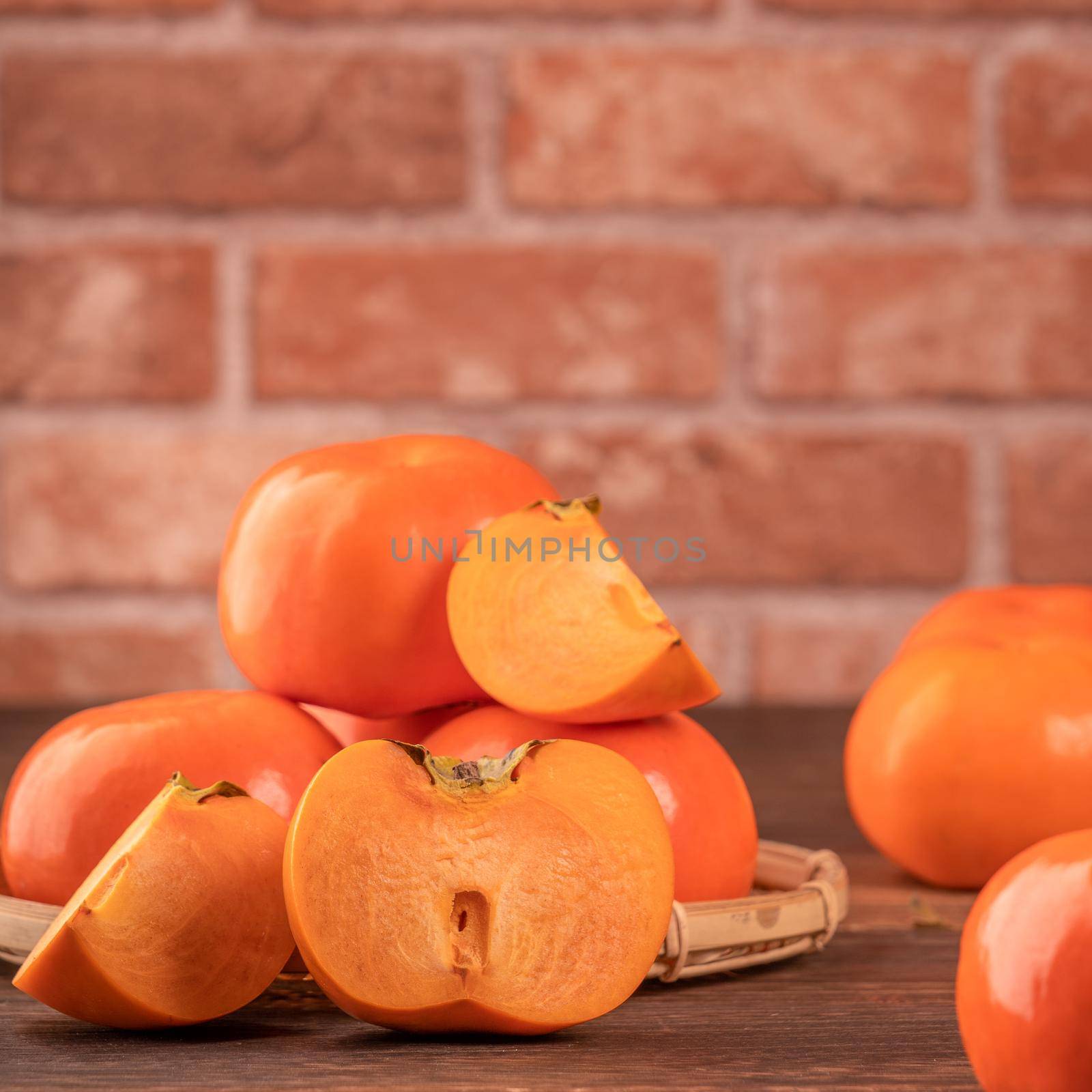 Fresh beautiful sliced sweet persimmon kaki on dark wooden table with red brick wall background, Chinese lunar new year fruit design concept, close up. by ROMIXIMAGE